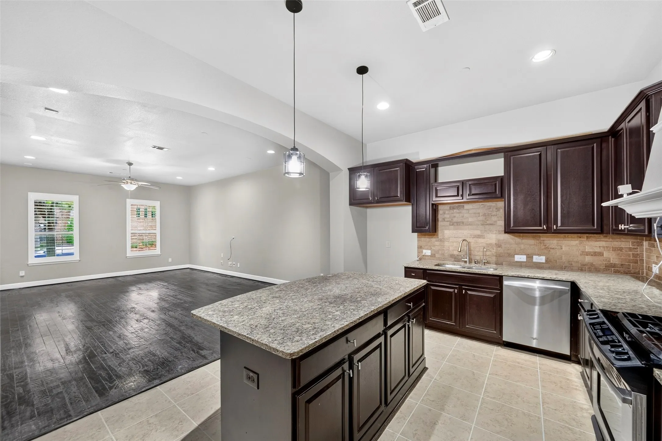 Kitchen featuring dark wood-finish cabinetry, stainless steel appliances, a tiled backsplash, and a central island with a stone-finish countertop