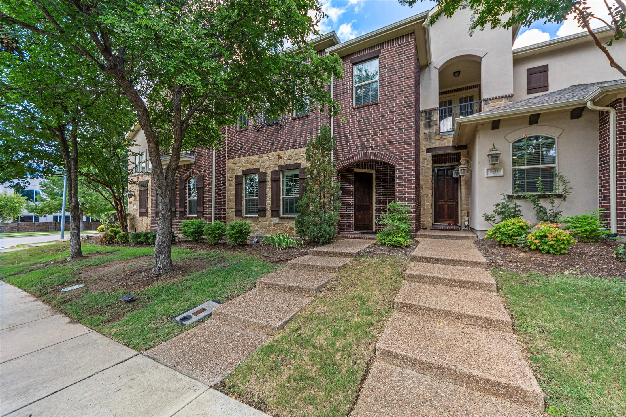 Brick and stucco exterior with stone accents, featuring arched entryways, dark wood doors, and decorative window shutters
