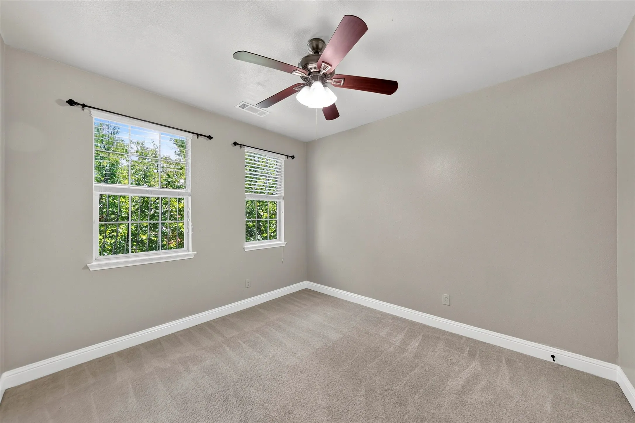 Neutral tone walls with white trim, wall-to-wall carpeting, two single-hung windows, and a ceiling fan with integrated lighting
