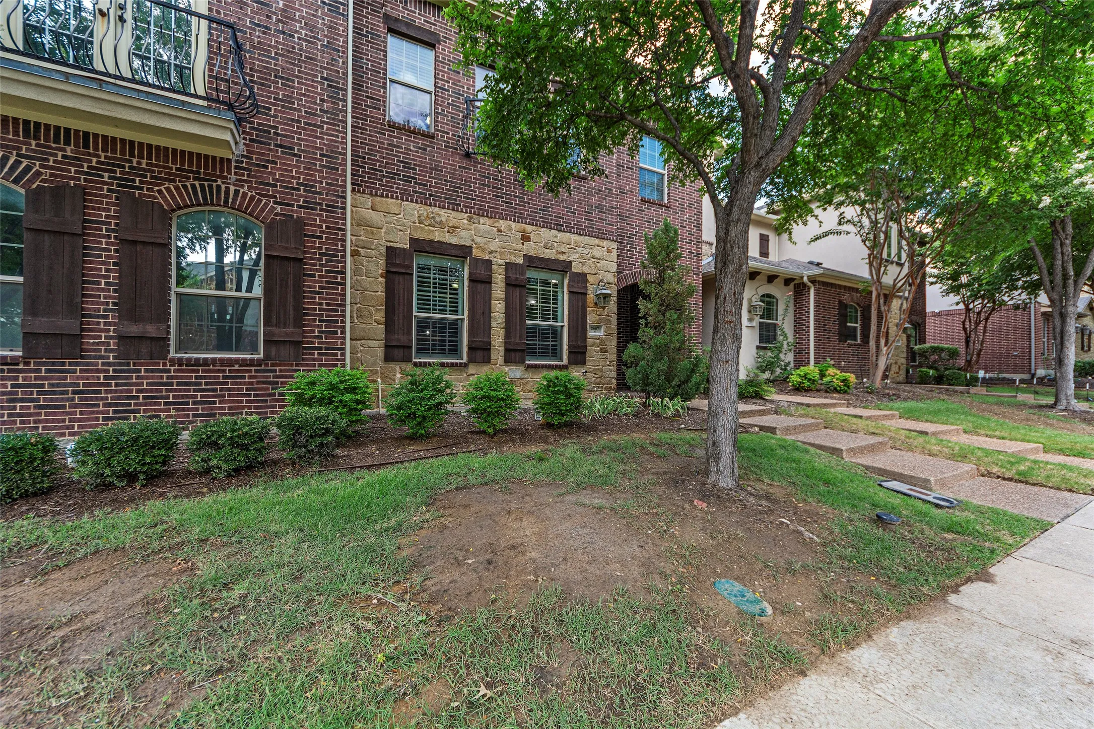 Brick and stone facade with dark shutters, arched window, and wrought iron balcony railing