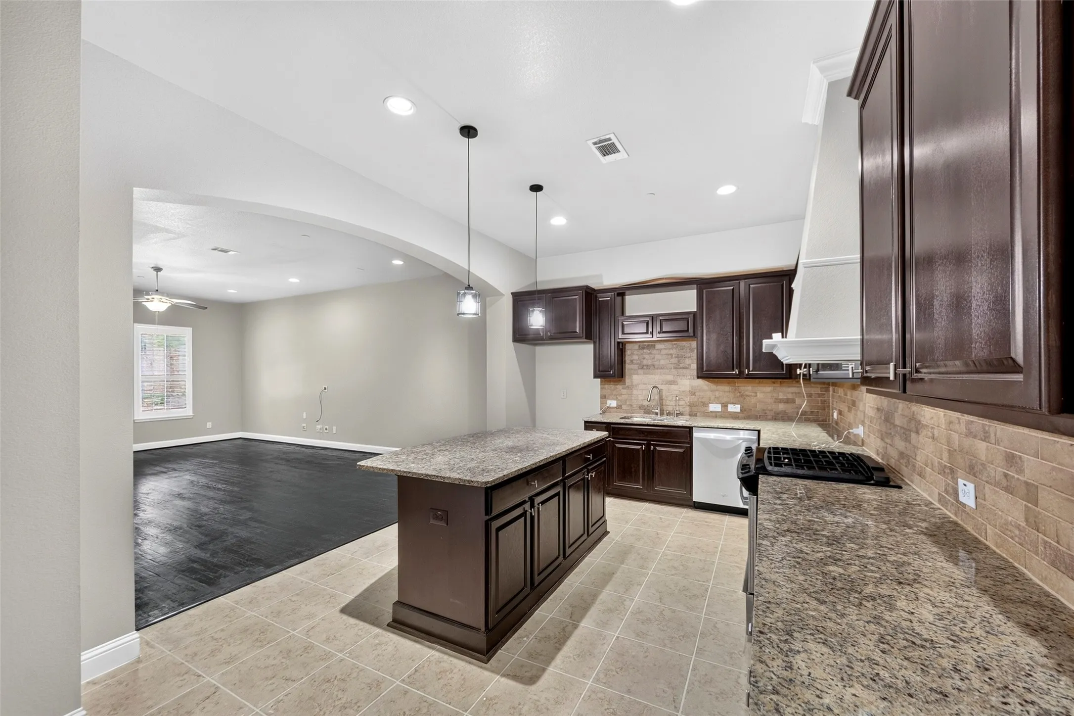 Kitchen featuring dark wood cabinetry, granite countertops, an island with pendant lighting, a tile backsplash, and tile flooring