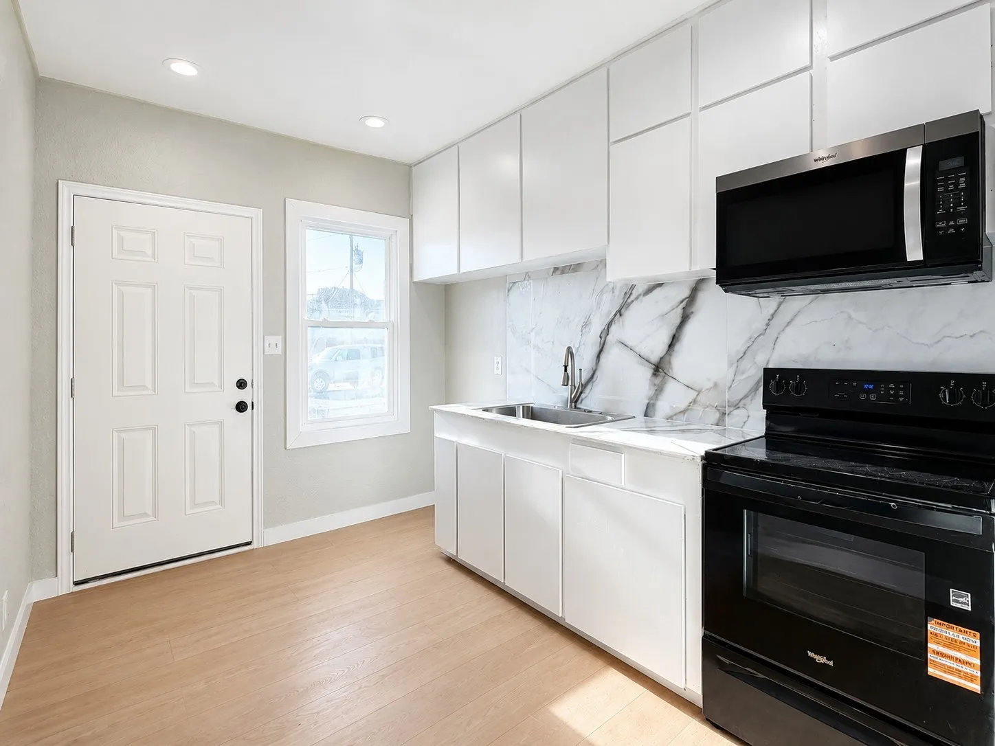 Kitchen featuring white cabinetry, a stainless steel sink, black appliances, a white and grey patterned backsplash, and wood-finish flooring