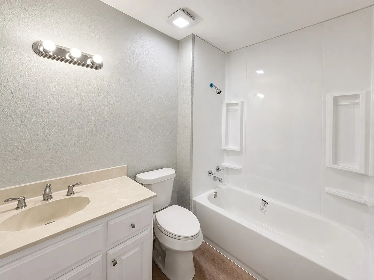 Bathroom featuring a white vanity with an integrated sink, a white bathtub with built-in shelving, a modern vanity light fixture, and wood-finish flooring