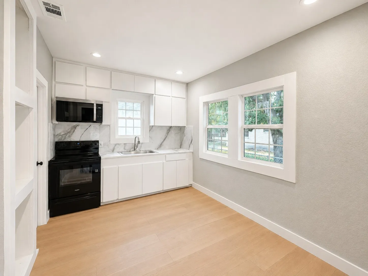 Kitchenette featuring white cabinetry, black appliances, stone-finish backsplash, wood-finish flooring, and recessed lighting