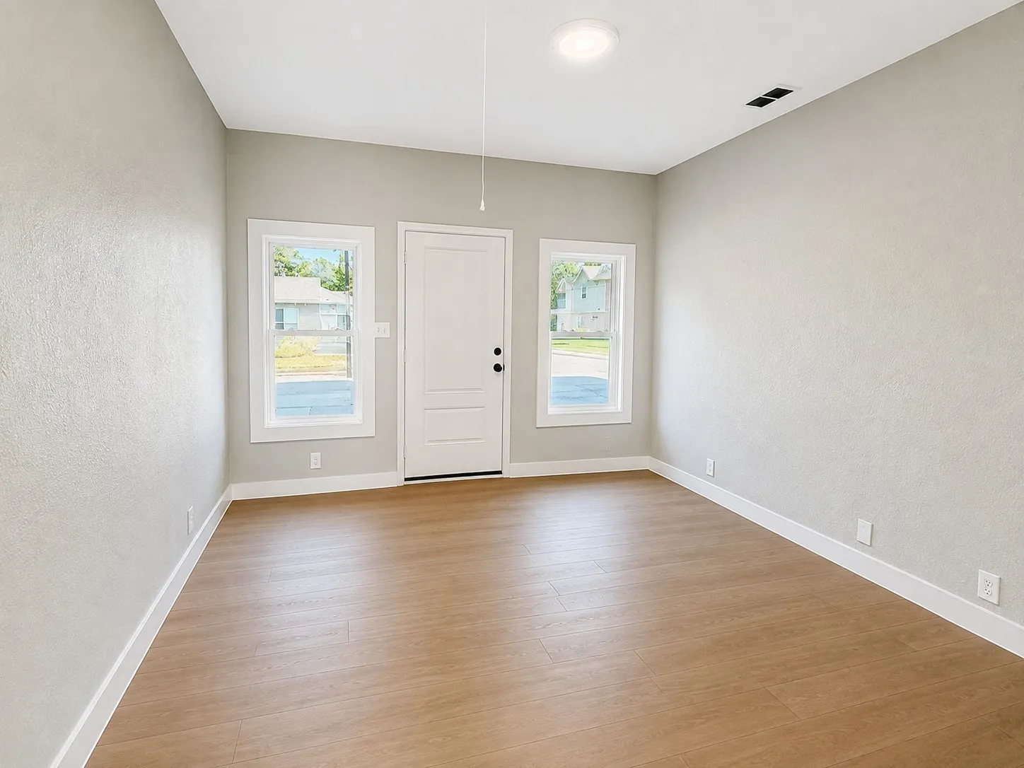 Wood-finish flooring, recessed ceiling lighting, textured neutral walls, white trim, and a paneled entry door