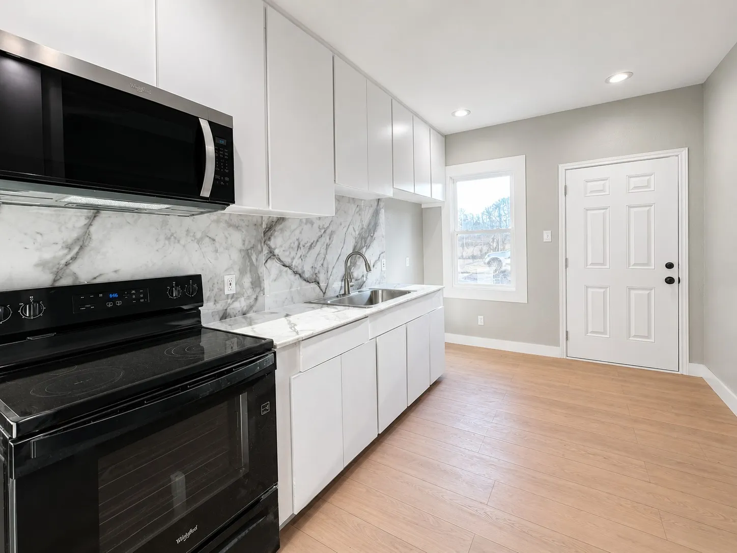 White cabinetry with a polished countertop, stainless steel sink, and a black oven