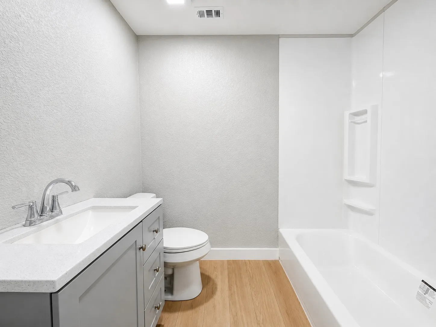 Modern vanity with an integrated sink, polished chrome faucet, wood-finish flooring, and a white bathtub with built-in shelving