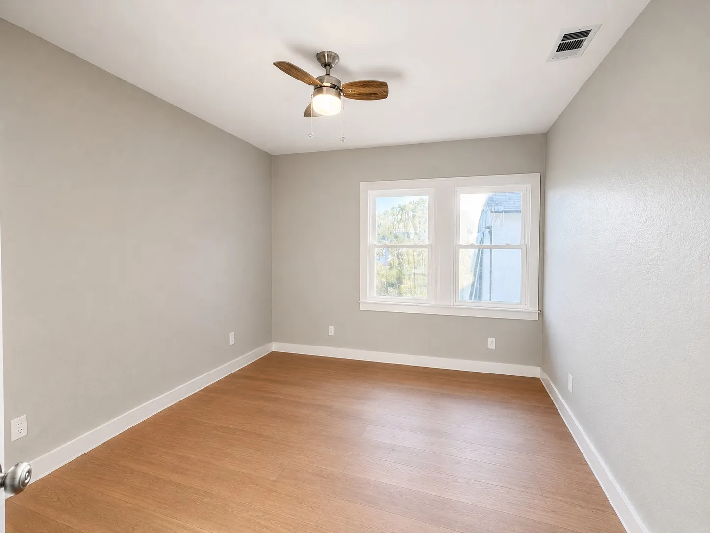 Wood-finish flooring with white trim, a double window, and a ceiling fan with integrated lighting
