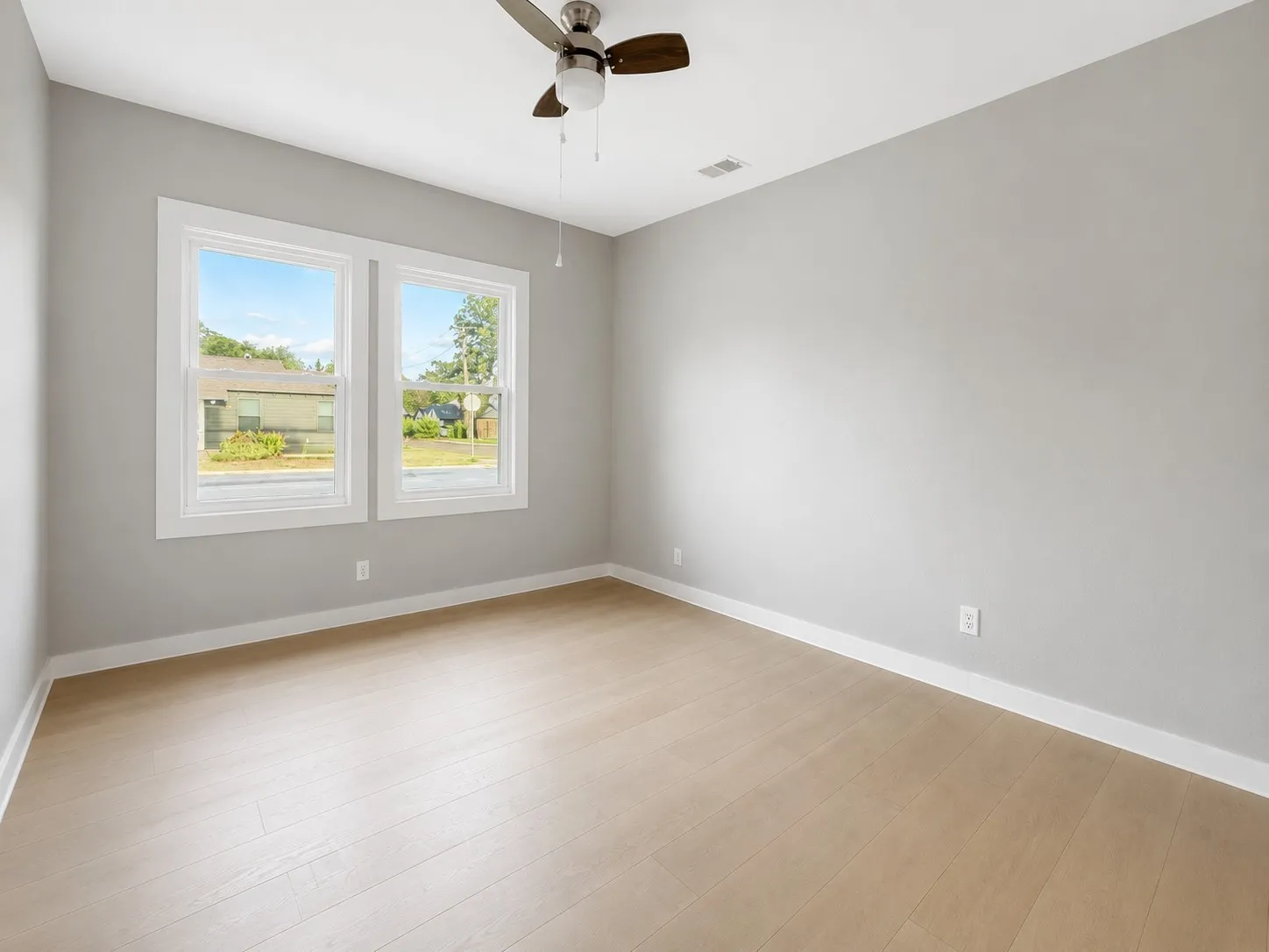 Two large windows with white trim, a ceiling fan, light wood-finish flooring, and light gray walls