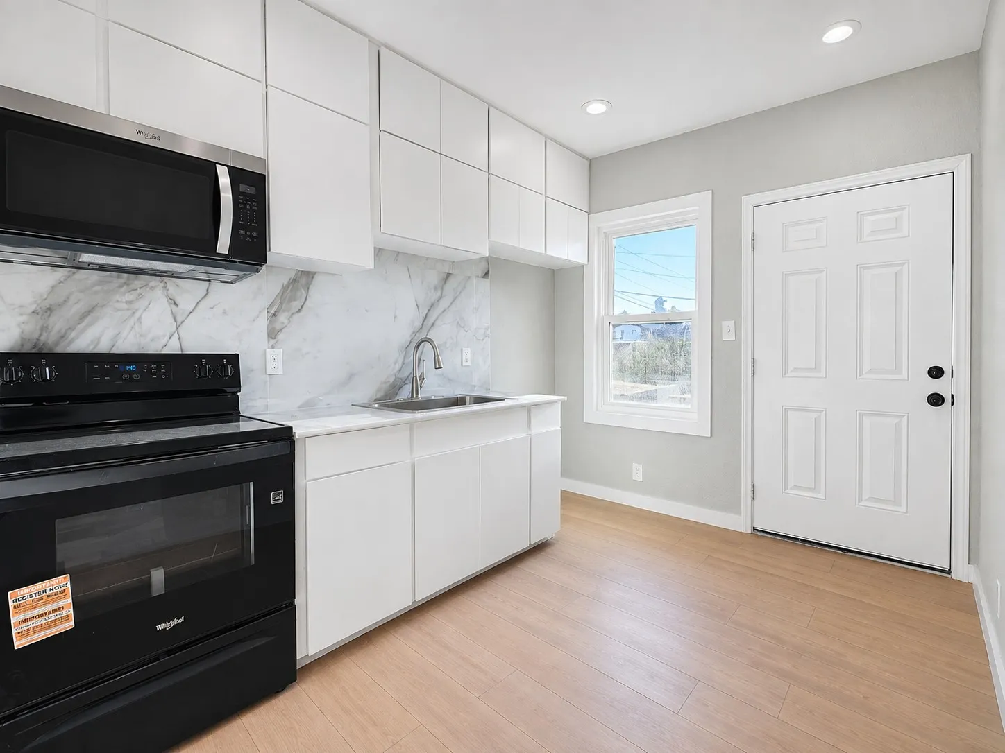 Modern kitchen featuring crisp white cabinetry, light wood-finish flooring, and a stainless steel over-the-range microwave