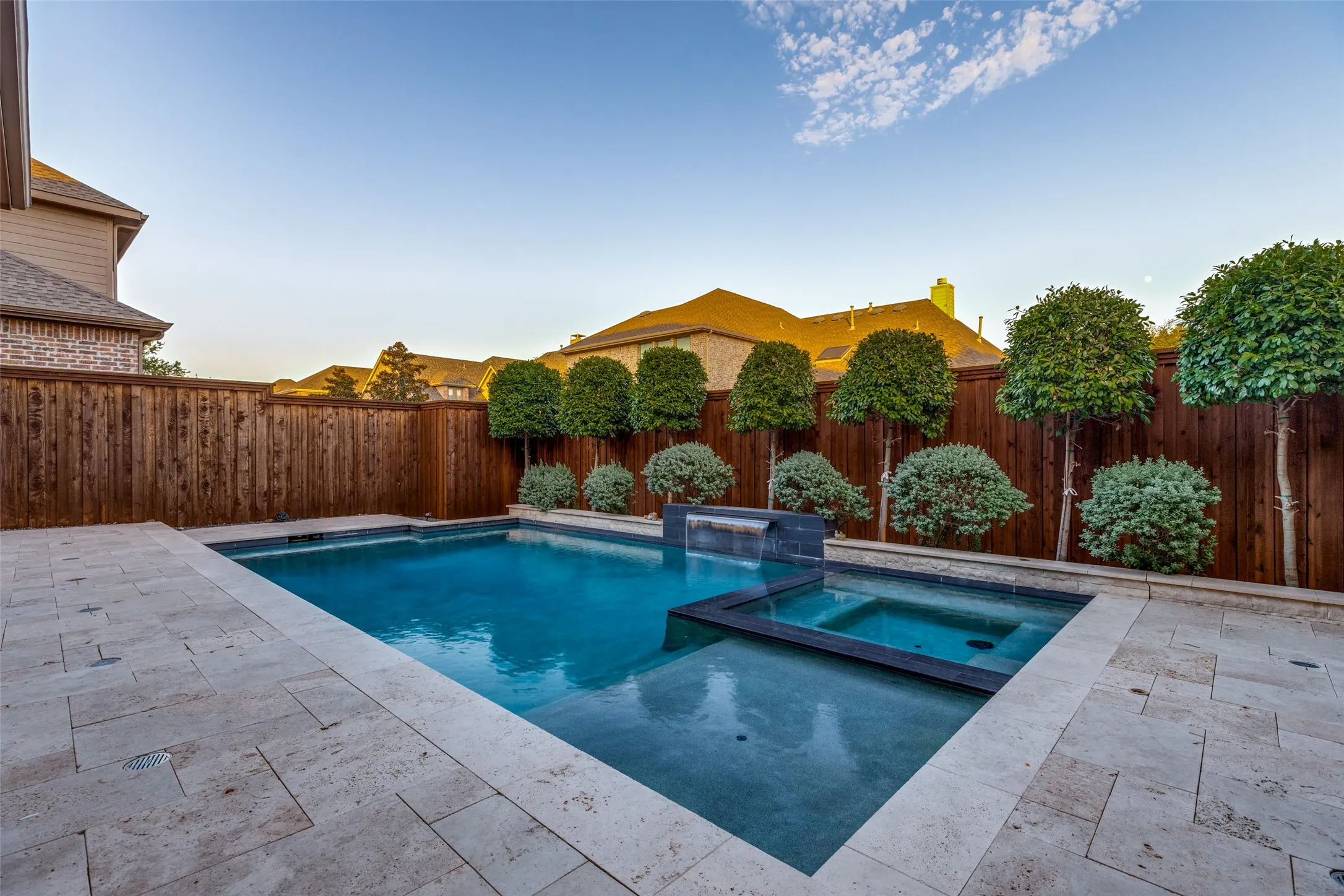 Private backyard oasis featuring a rectangular pool with an integrated spa, a tiered water feature, and extensive paver patio