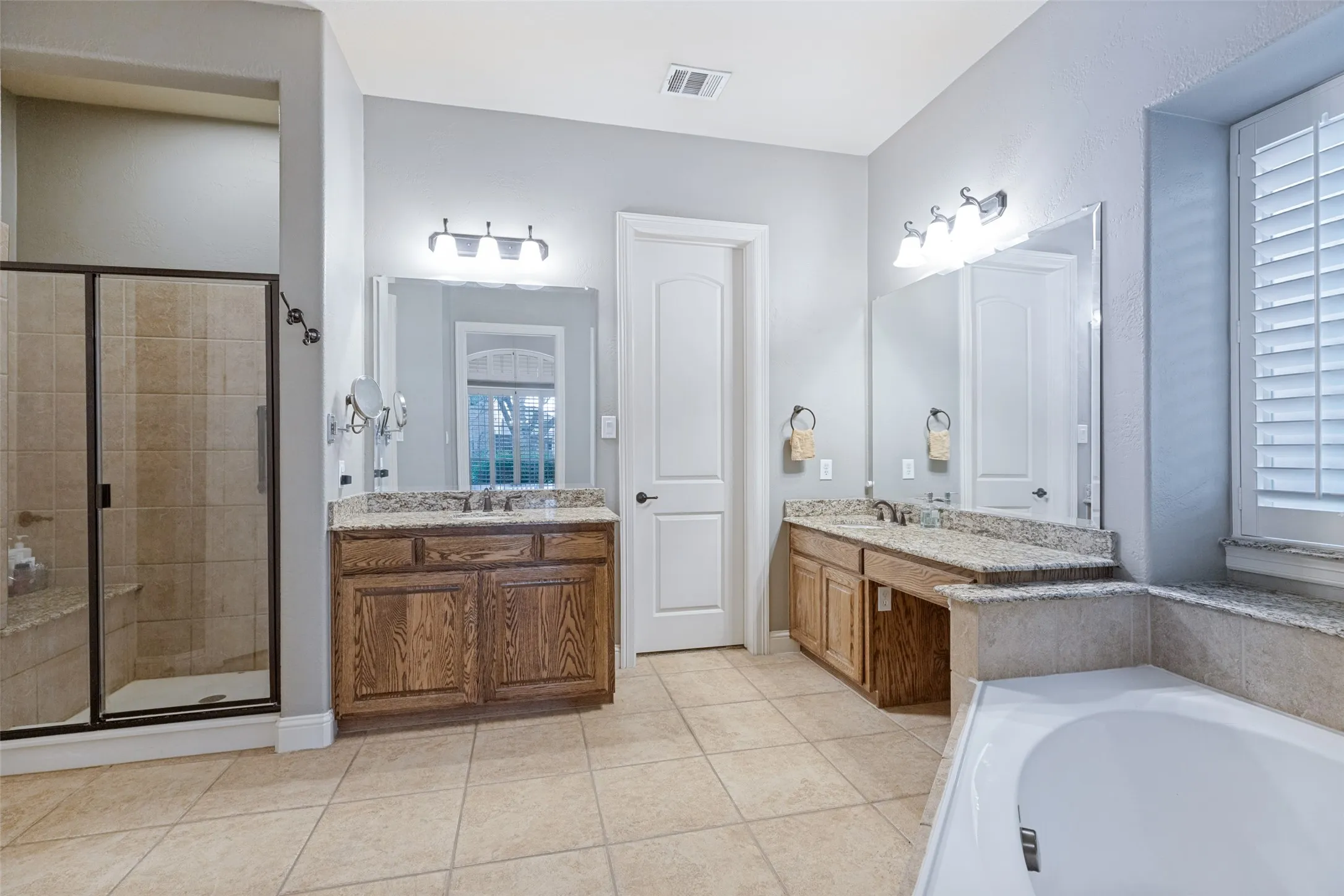 Dual vanities with stone countertops, tiled walk-in shower with bench, built-in bathtub, and ceramic tile flooring