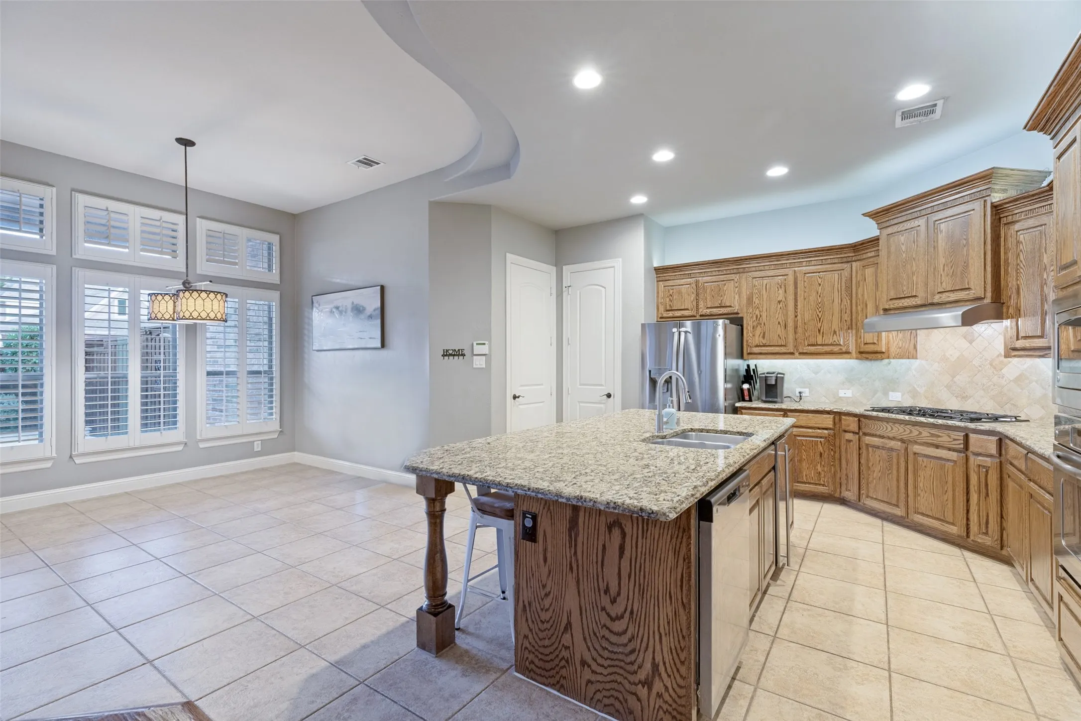 Kitchen with wood cabinetry, granite countertops, tile flooring, recessed lighting, and stainless steel appliances