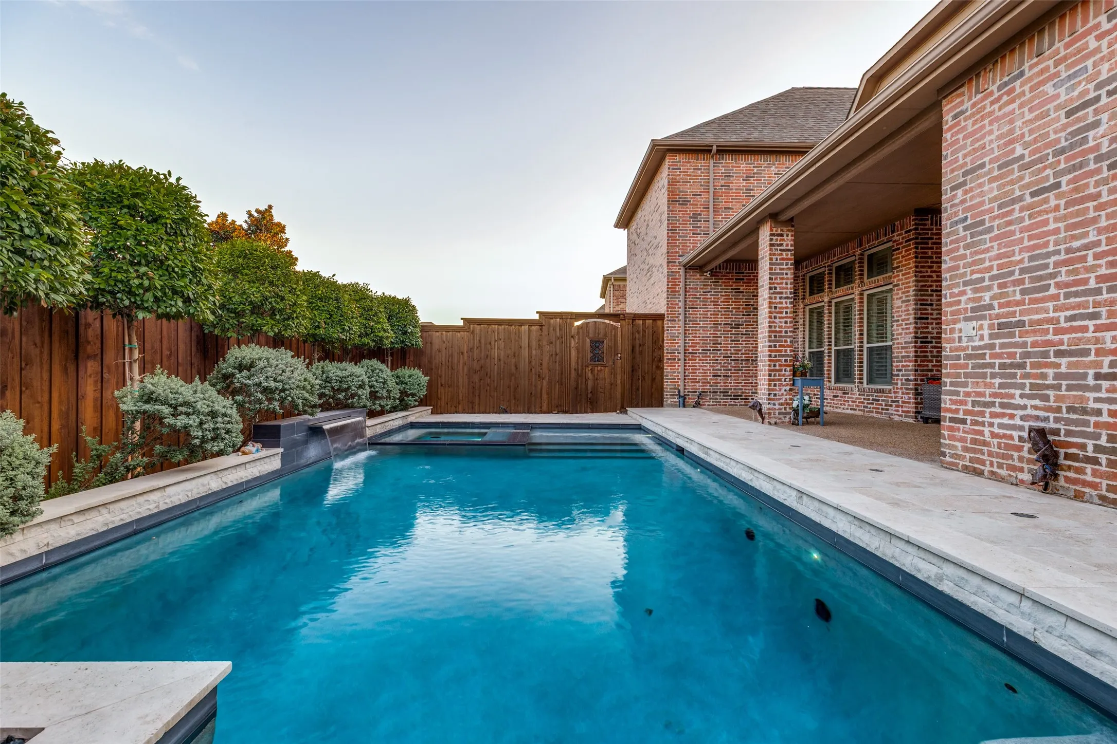 Brick exterior with a covered patio overlooking a swimming pool and attached spa