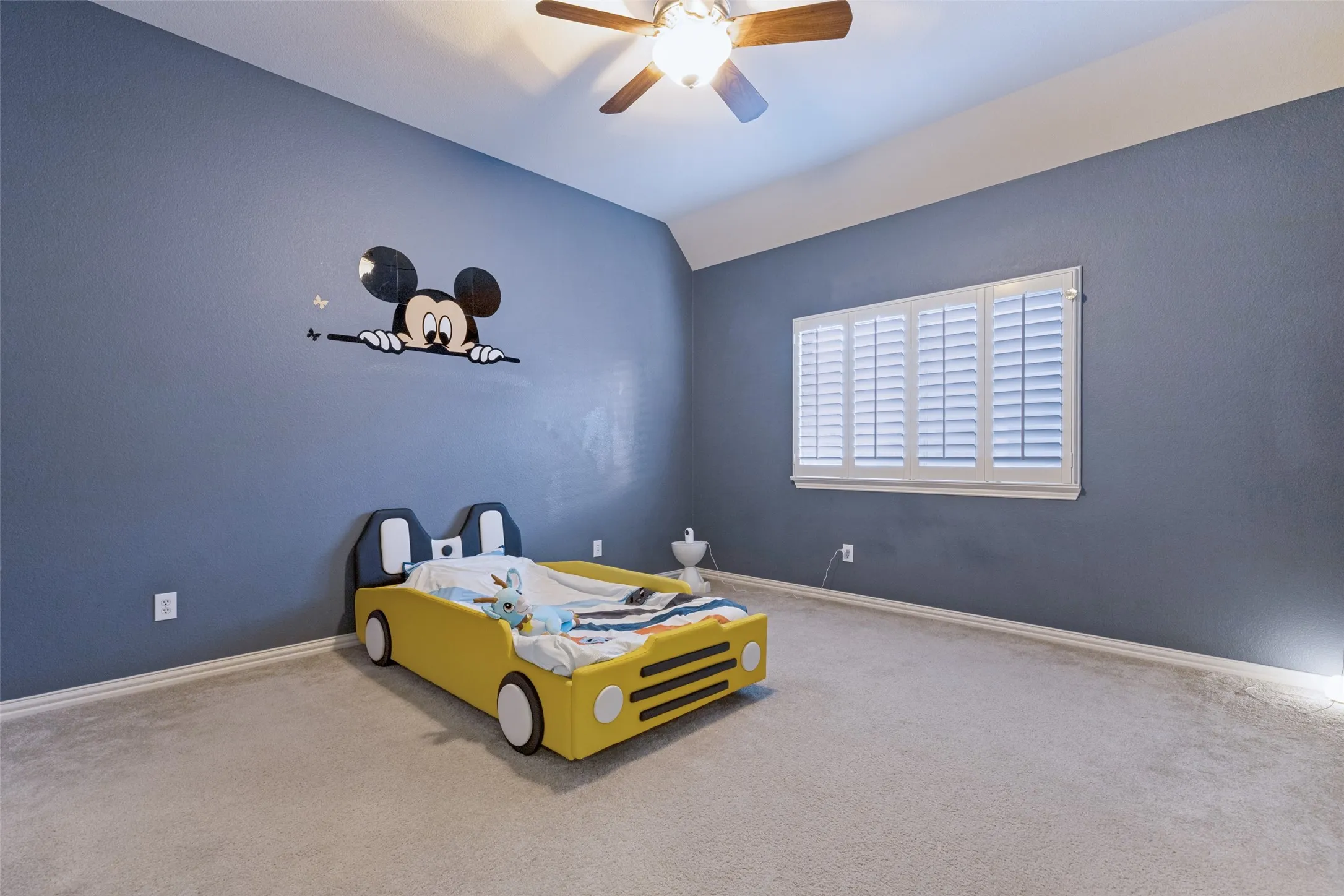 Recessed window with white plantation shutters, light gray wall-to-wall carpeting, and a ceiling fan with light fixture
