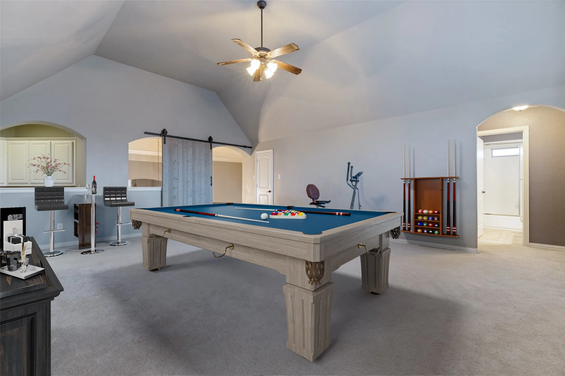 Vaulted ceiling with a ceiling fan, recessed wet bar with built-in cabinetry, and a barn door entry