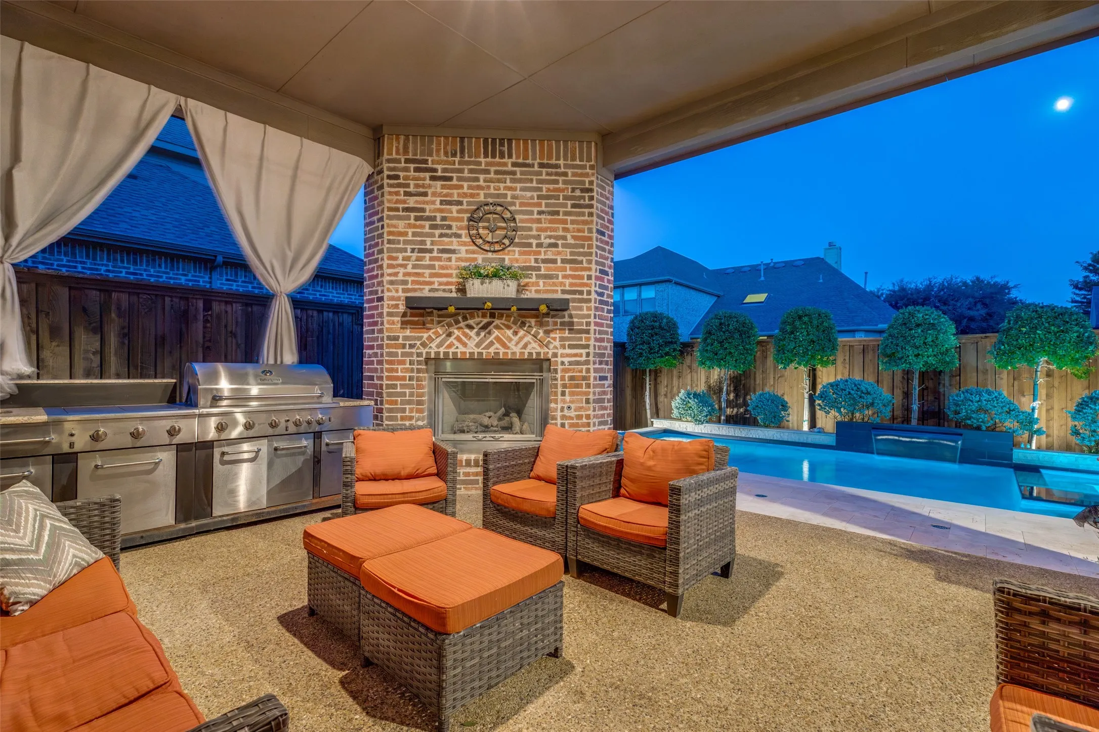 Covered patio with brick fireplace, built-in outdoor kitchen, gravel-finish flooring, and a swimming pool with integrated water features