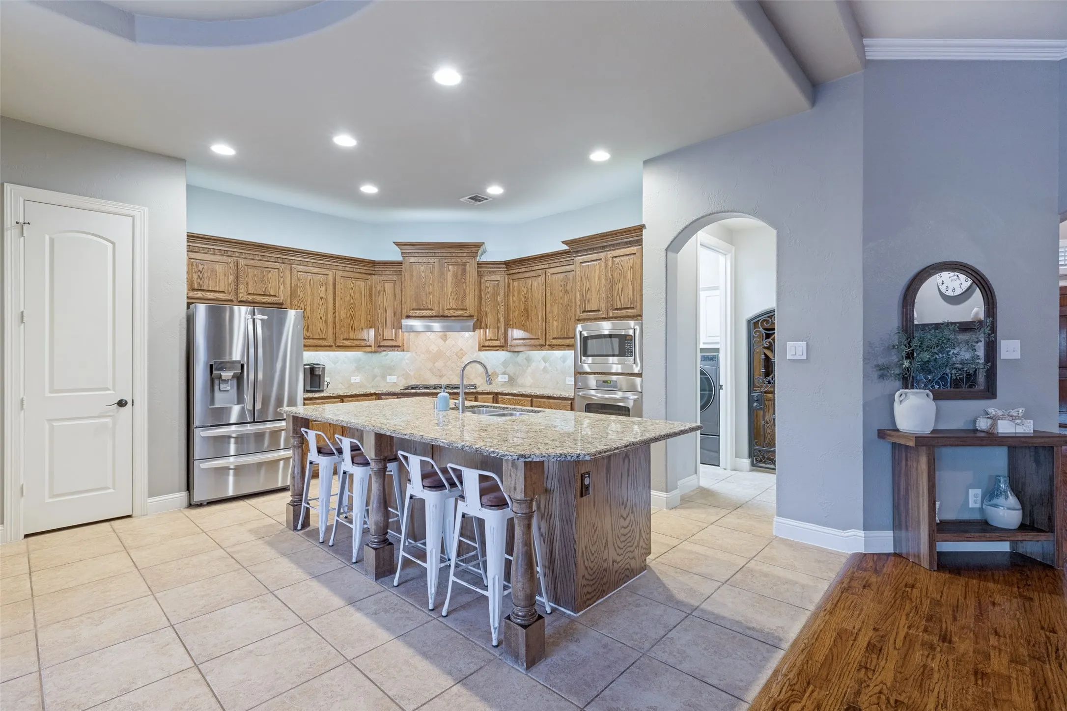 Kitchen featuring a large island with seating, stainless steel appliances, wood cabinetry, tile flooring, and an arched doorway