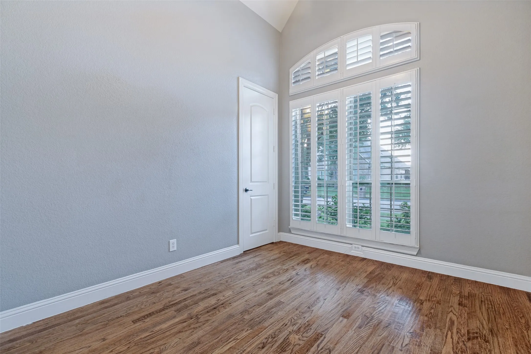 Hardwood flooring, vaulted ceiling, arched window, plantation shutters, and a paneled door