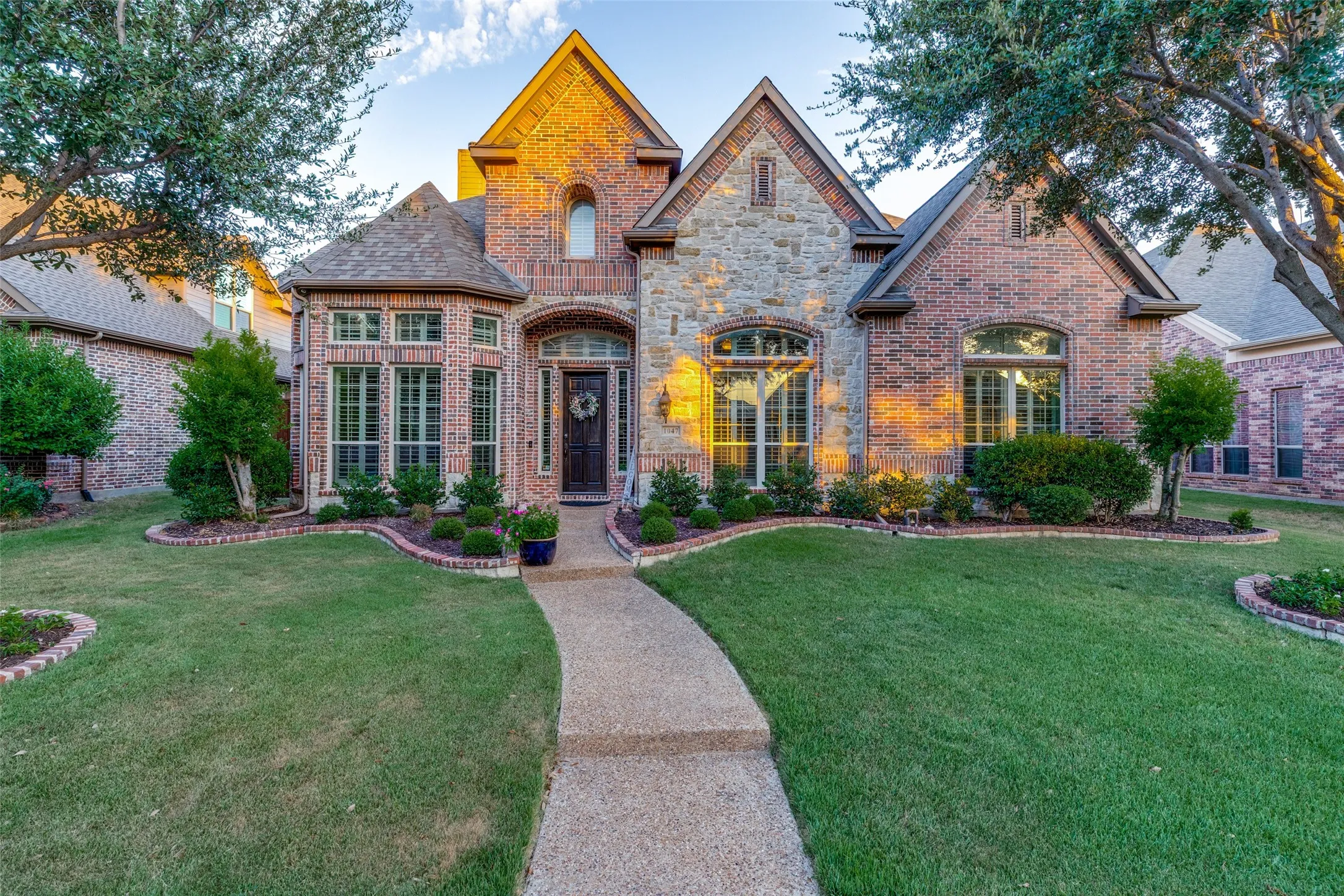 Brick and stone exterior with architectural gables, a curved stone pathway, and manicured landscaping