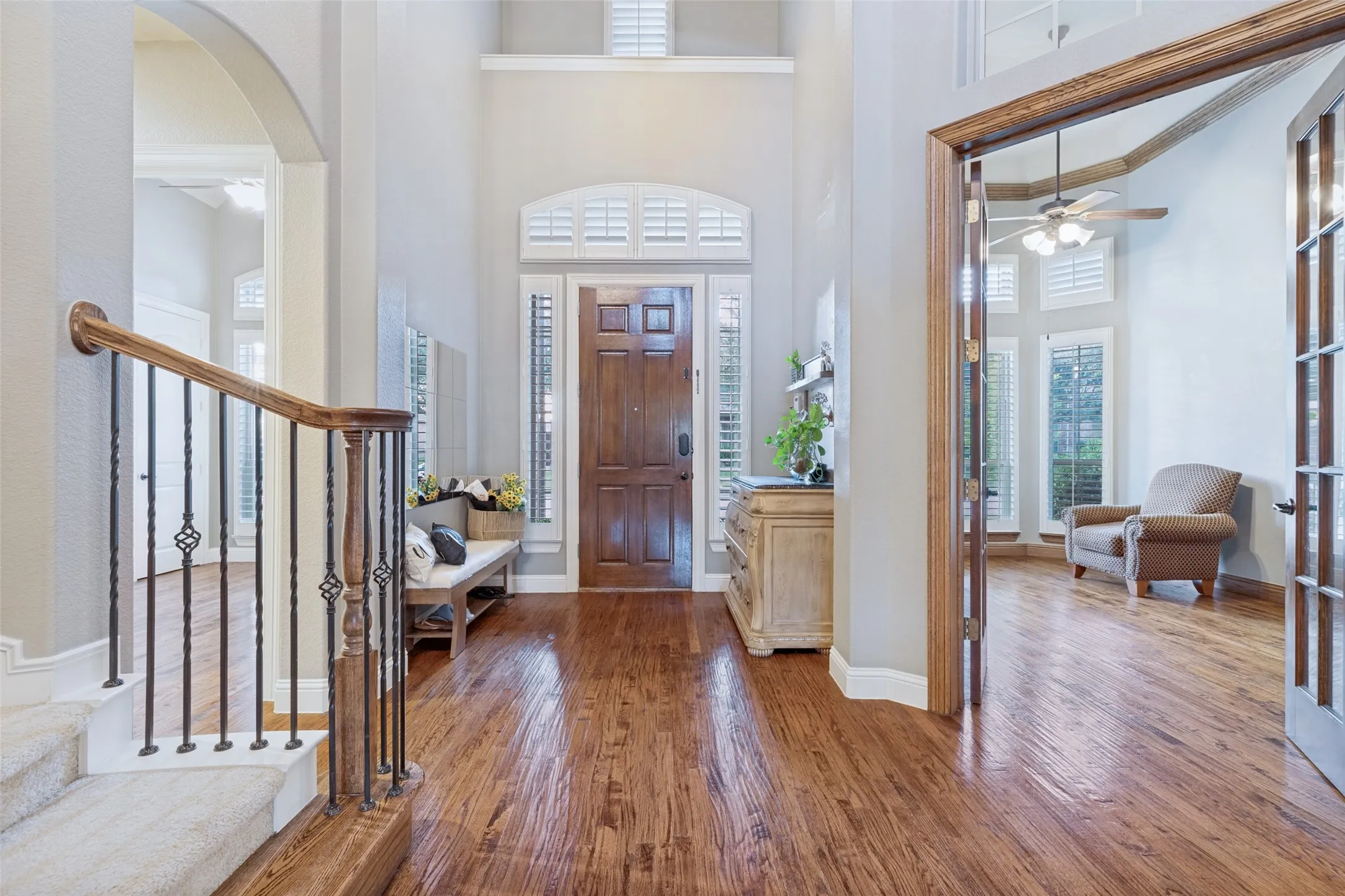 Two-story foyer with wood-finish flooring, a solid wood entry door, and plantation shutters