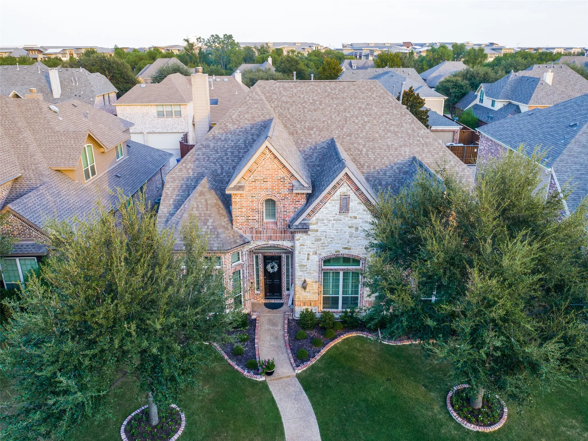 Exterior featuring a brick and stone facade, gabled roofline, arched entry, and mature landscaping