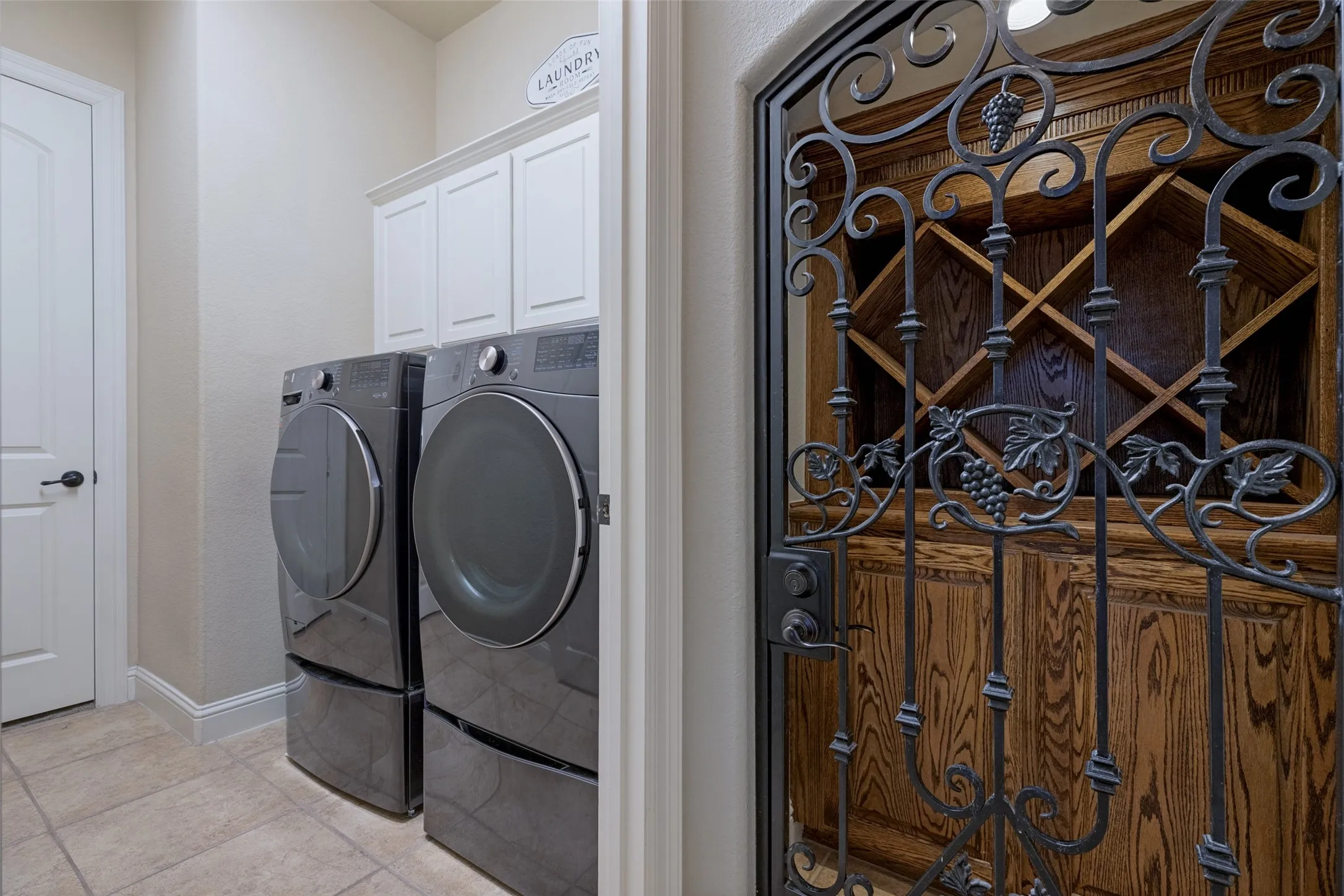Custom ironwork gate with grape detailing, wood-finish wine storage, built-in laundry cabinetry, and tiled flooring