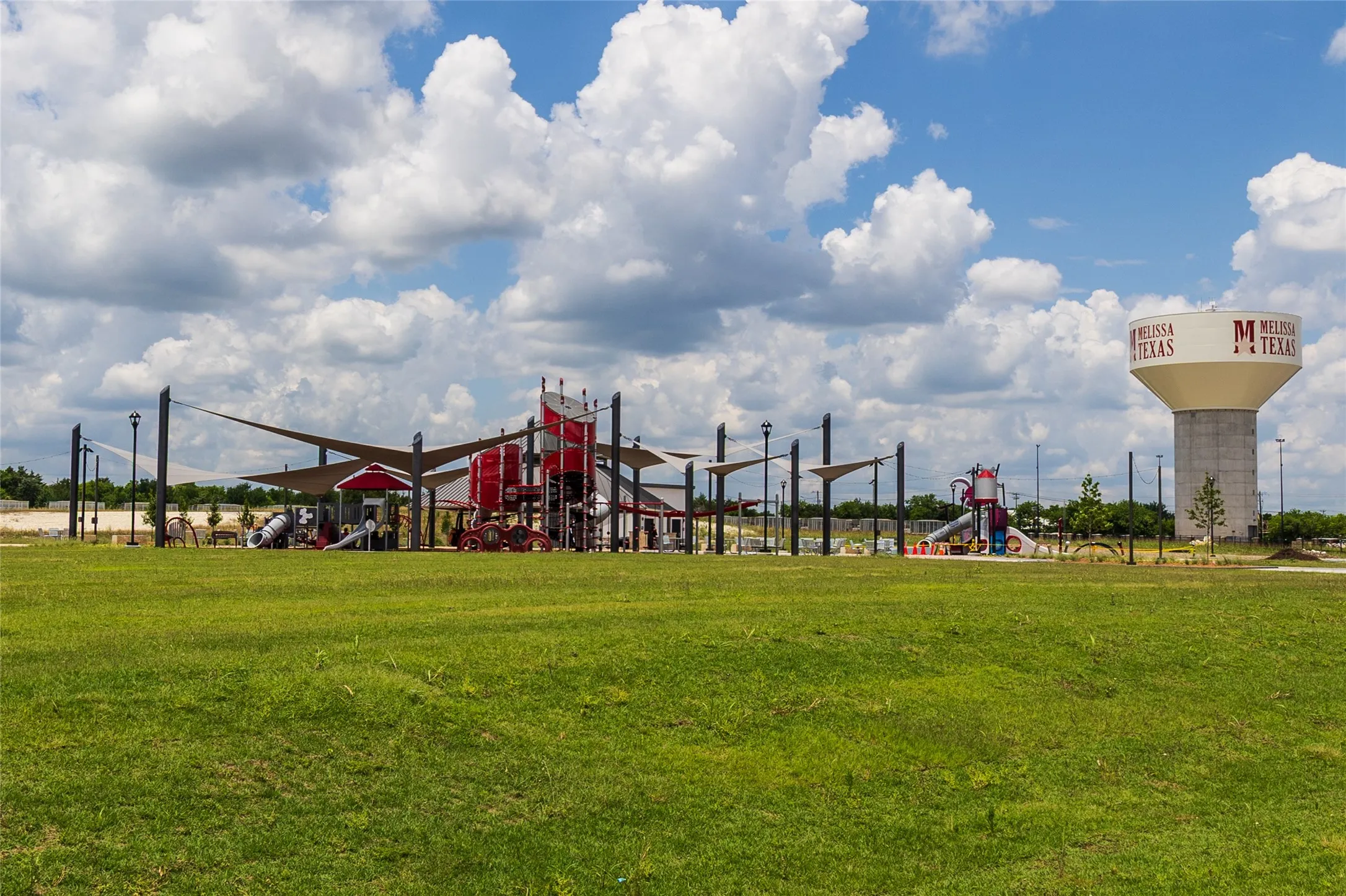 Expansive green space featuring a large playground with shade structures and a water tower