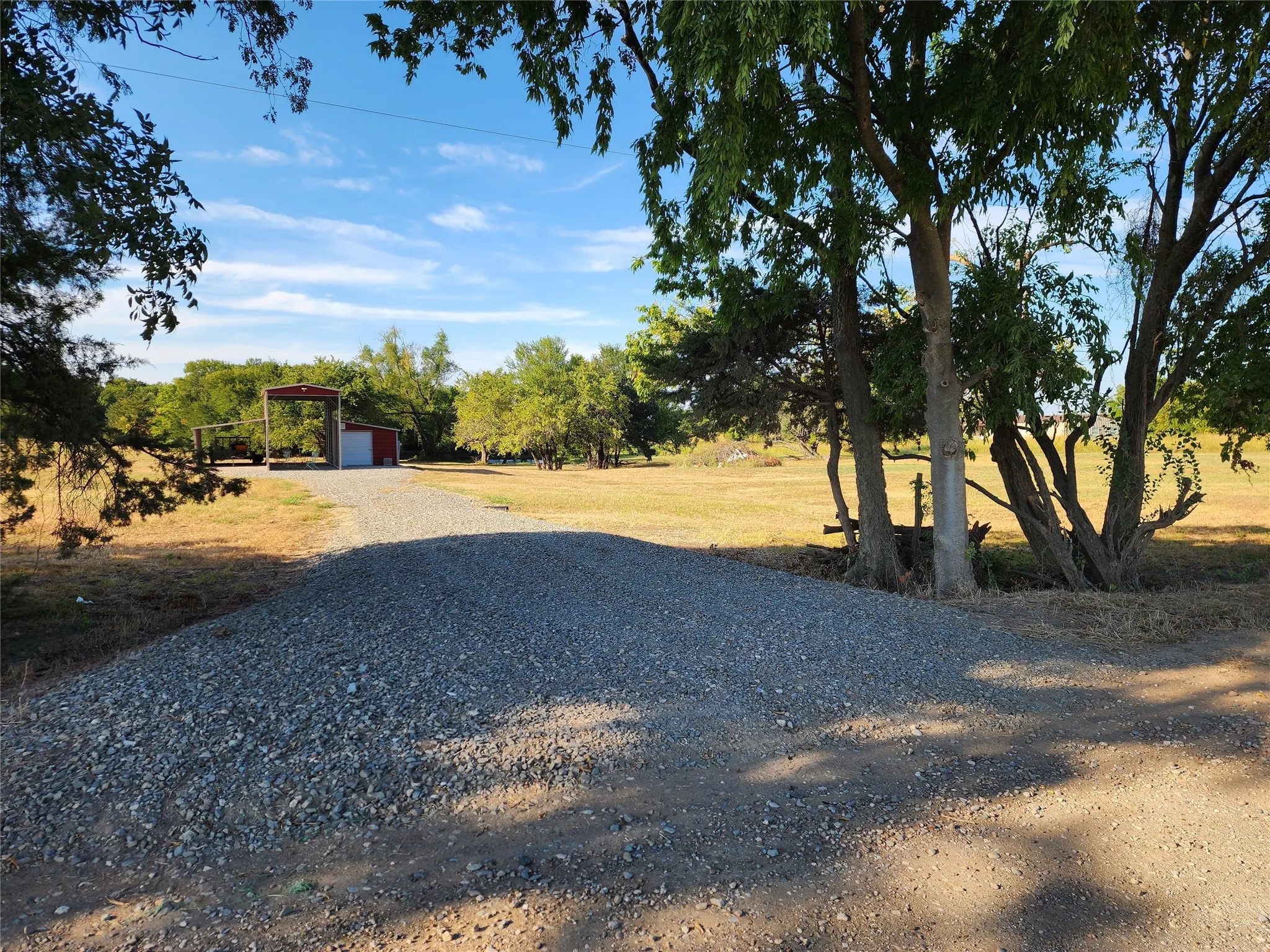 Gravel driveway leading to a red metal structure with an open carport and enclosed storage