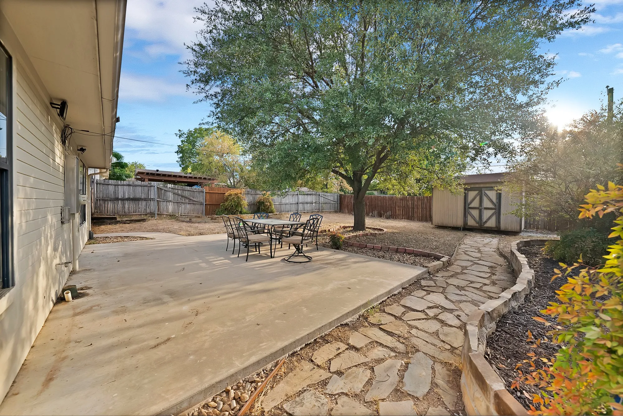 Spacious concrete patio with a flagstone pathway, mature shade tree, and wood privacy fencing