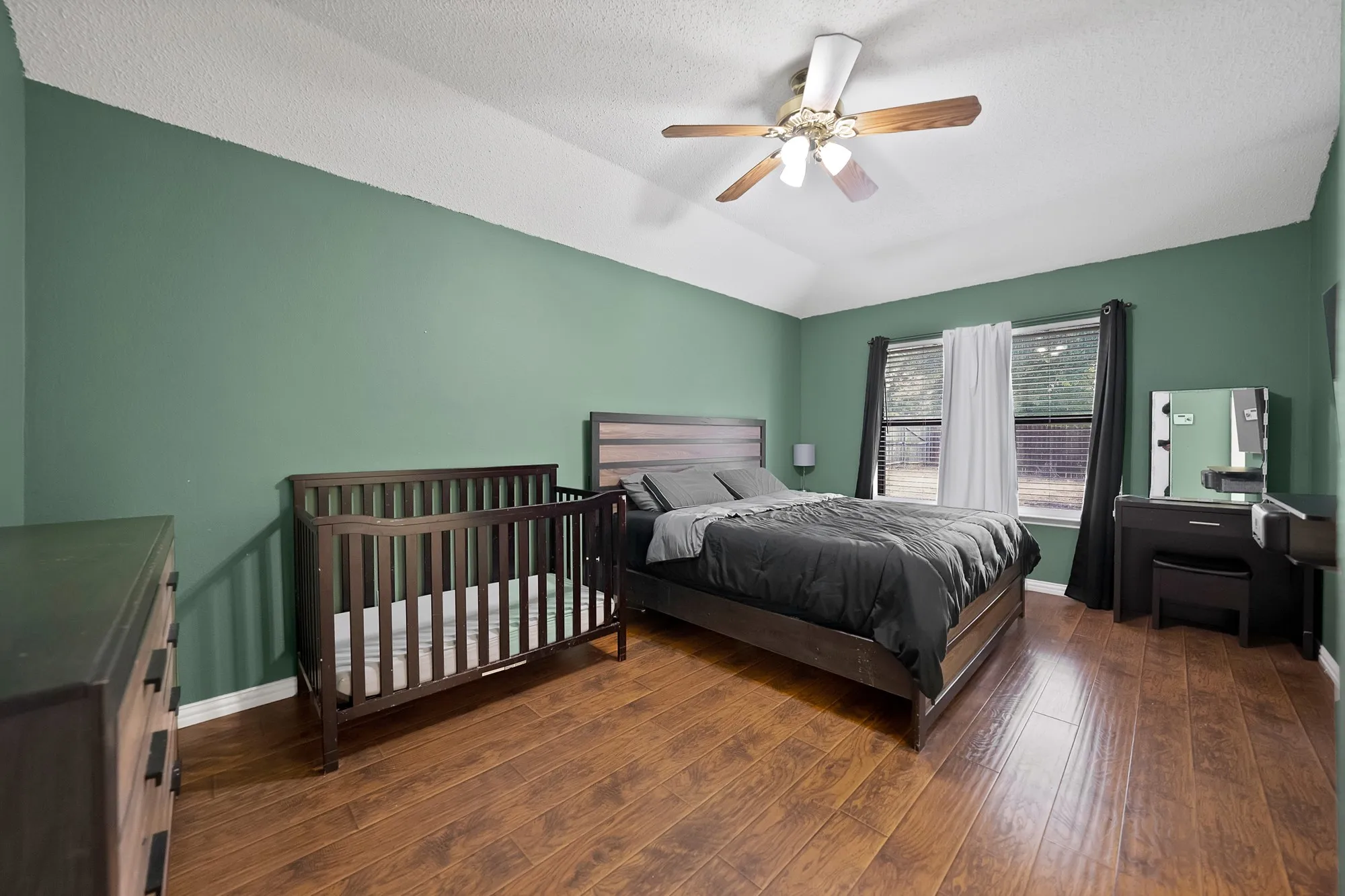 Vaulted ceiling with a ceiling fan, wood-finish flooring, two windows with blinds, and green painted walls