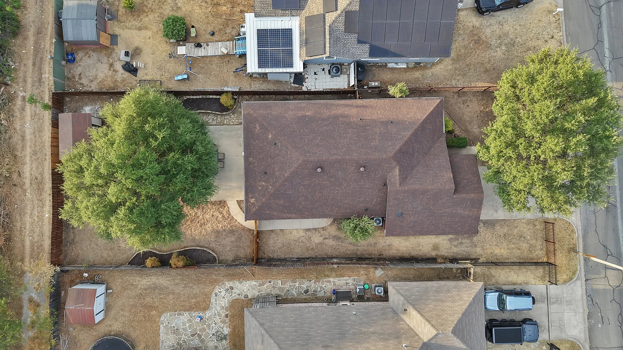 Gabled roofline, mature trees, fenced backyard, concrete patio, landscaped garden beds