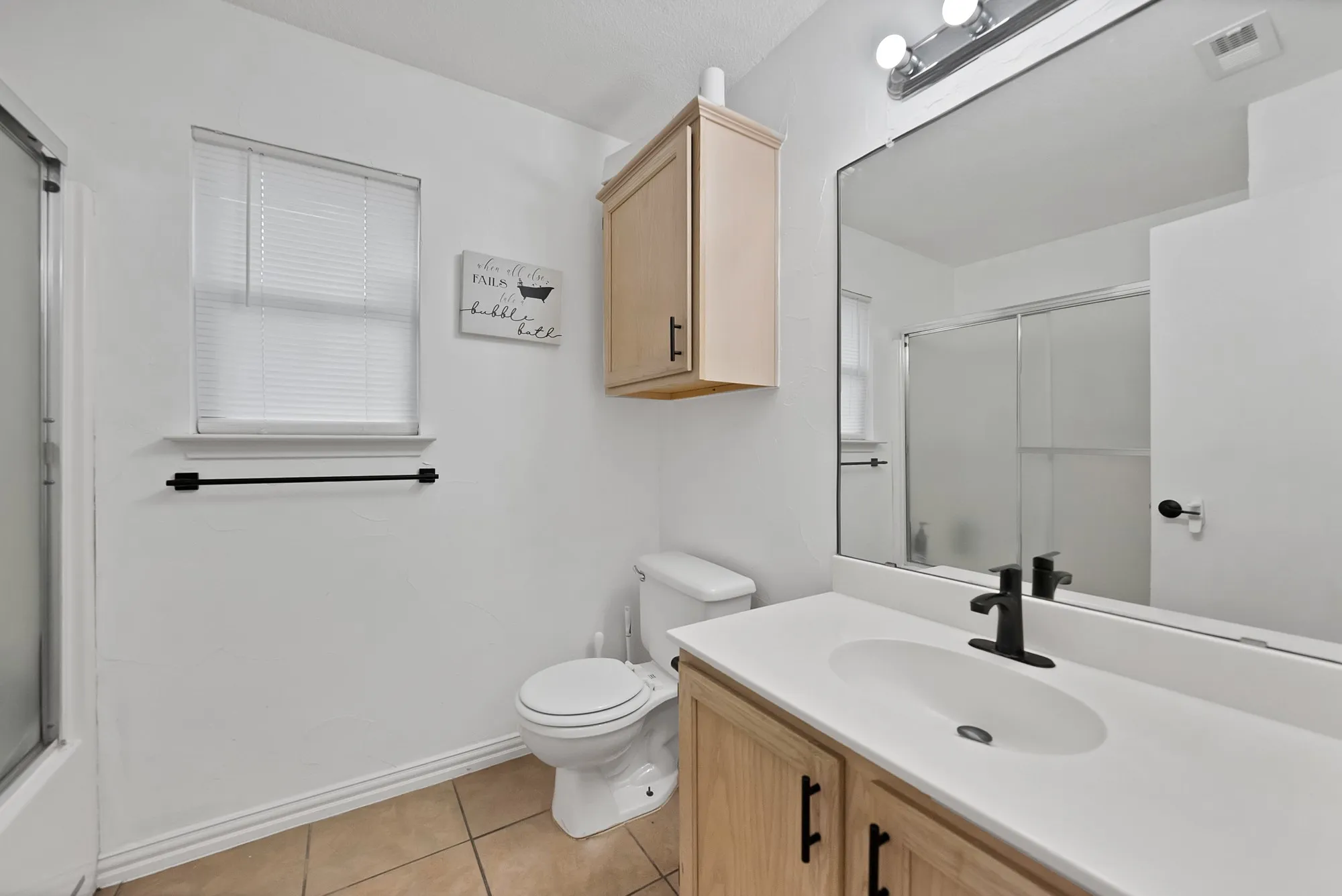 Bathroom featuring a single vanity with a white countertop, wood-finish cabinetry, a matte black faucet, and a large wall mirror