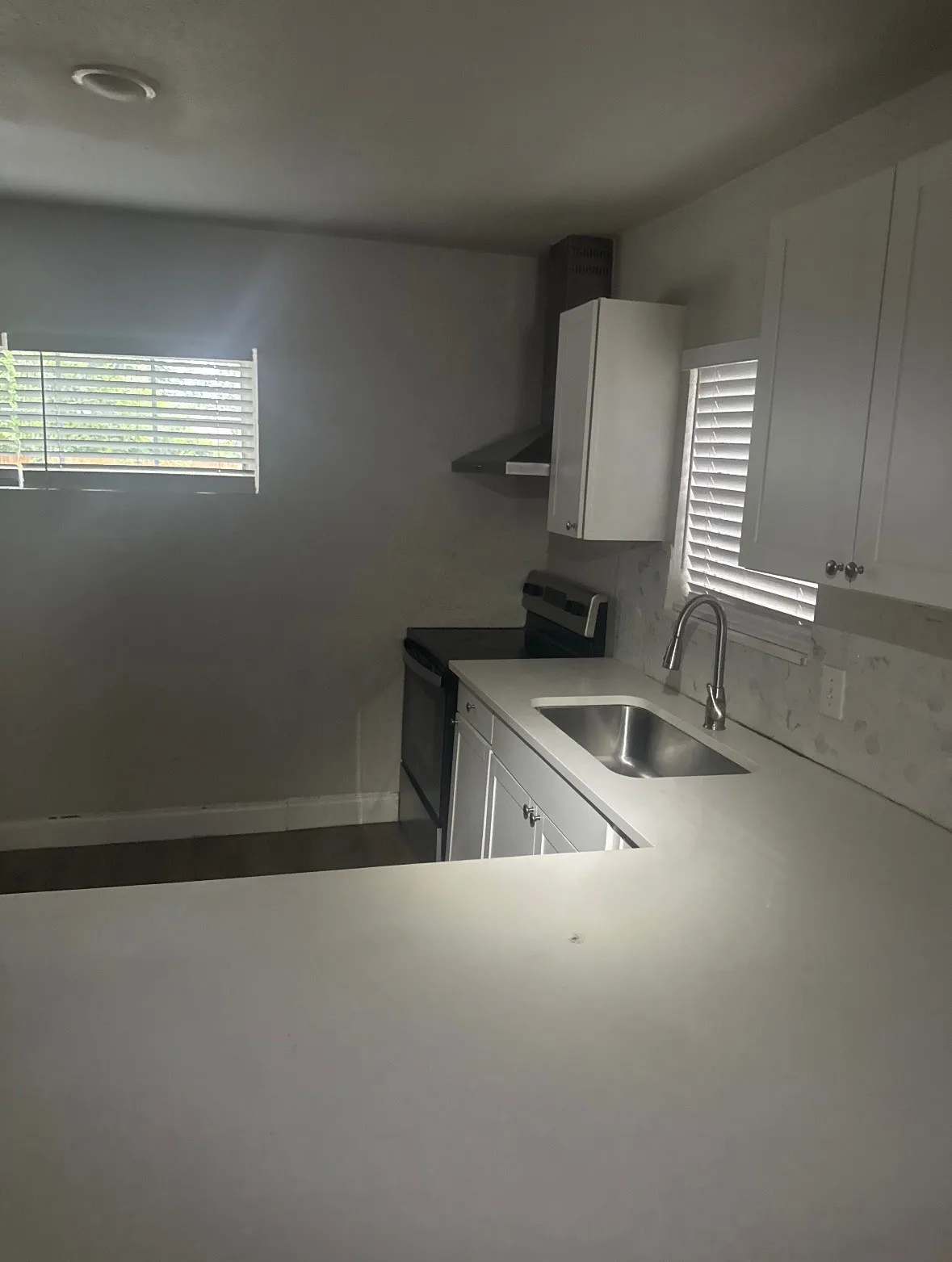 White cabinetry, stainless steel sink, contemporary faucet, built-in range hood, and solid surface countertops