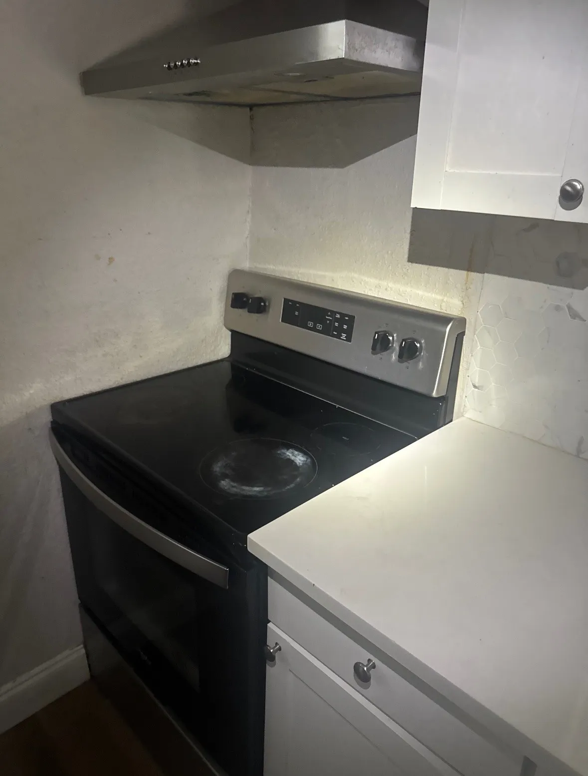 Stainless steel range hood over a black electric range with a smooth cooktop, accompanied by white cabinetry and a light-toned countertop