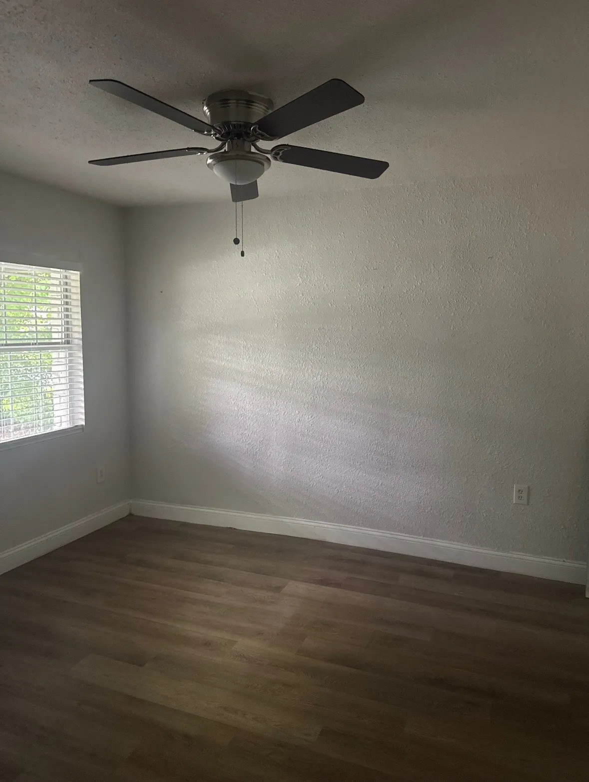 Wood-finish flooring with white trim and a ceiling fan with integrated lighting