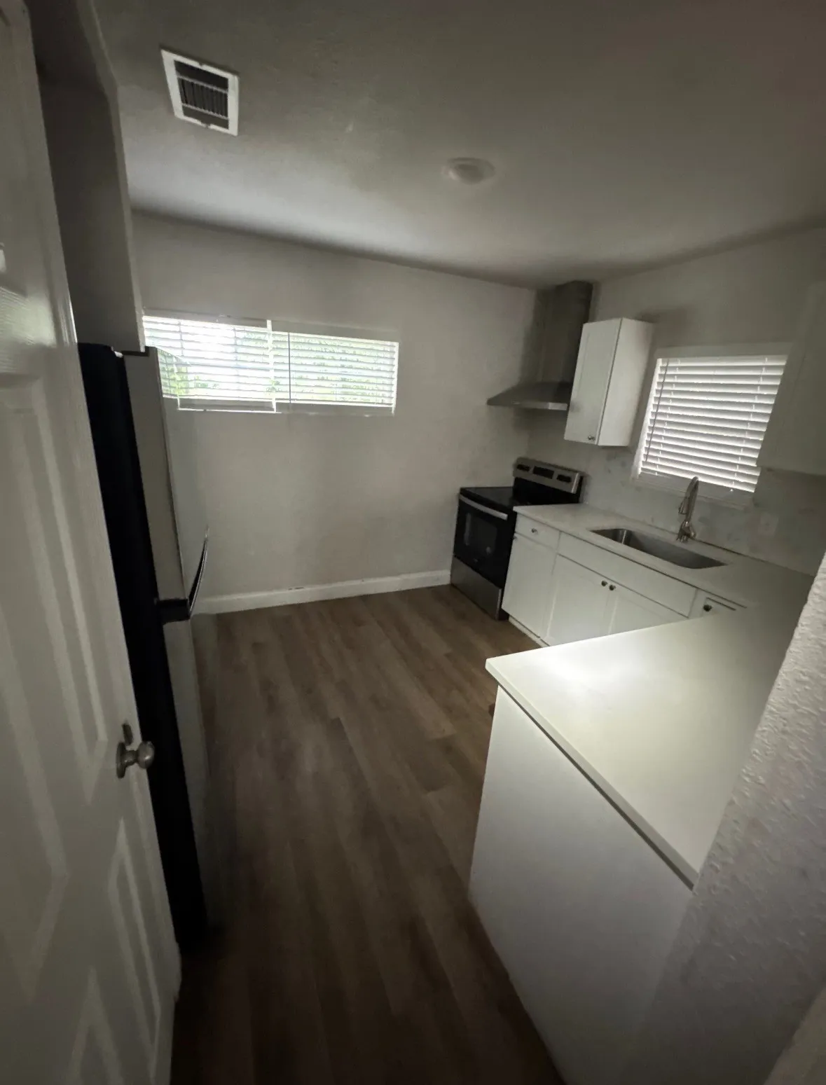 White cabinetry with metal hardware, wood-finish flooring, white countertops, stainless steel appliances, and a stainless steel range hood