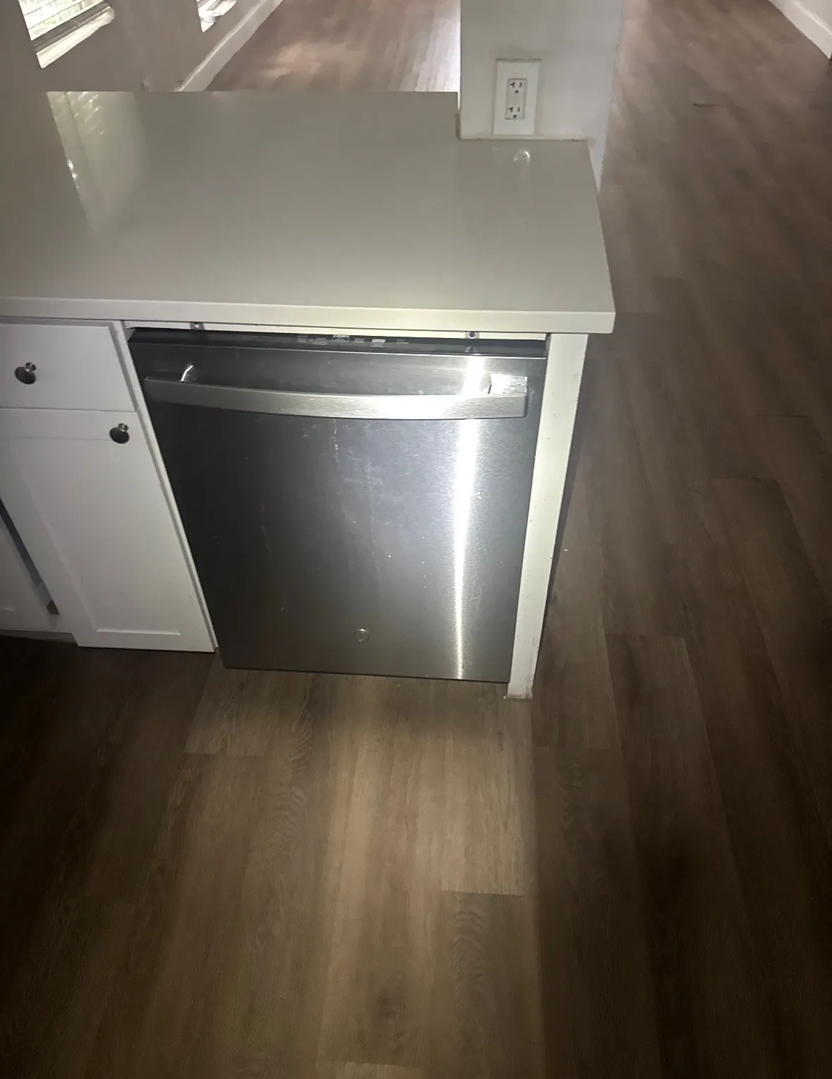 White cabinetry with dark hardware and a stainless steel dishwasher, complemented by a light-toned countertop and wood-finish flooring