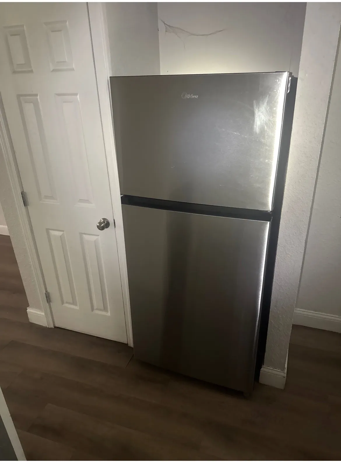 Stainless steel top-freezer refrigerator, wood-finish flooring, and a paneled interior door