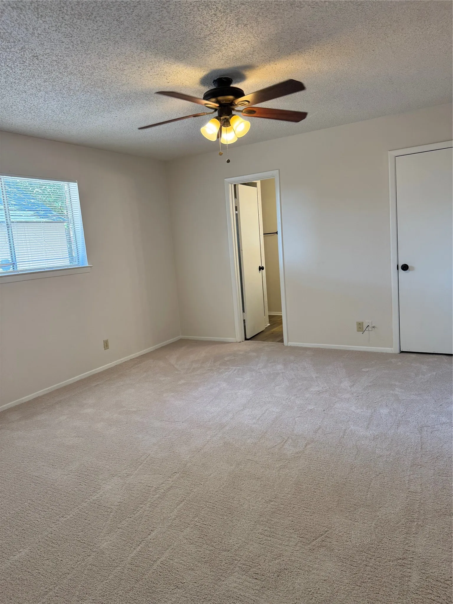 Neutral tone wall paint, light-colored carpeting, a ceiling fan with integrated lighting, and a white interior door with a black knob