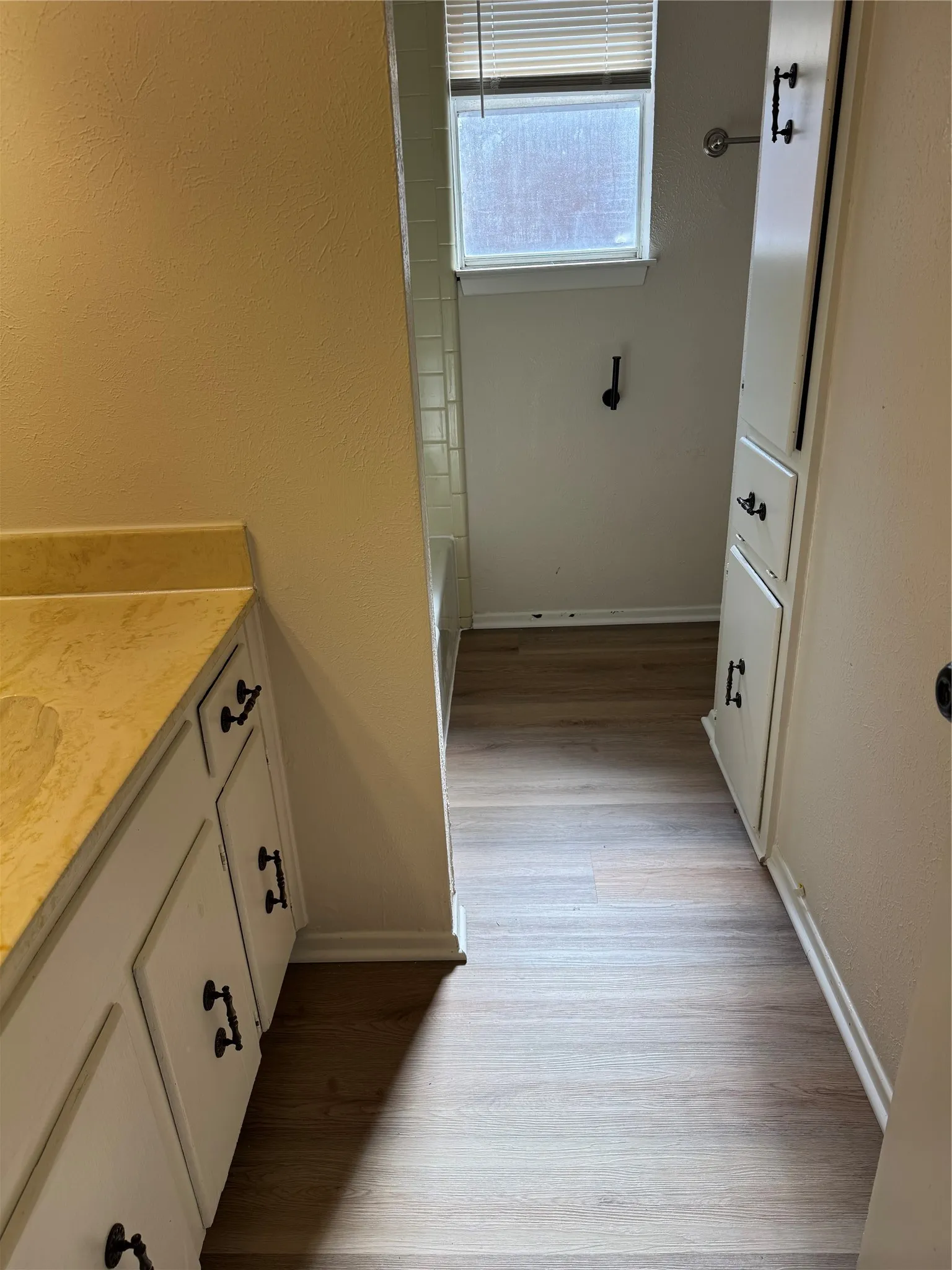 Wood-finish flooring, built-in cabinetry with black hardware, and a window with blinds