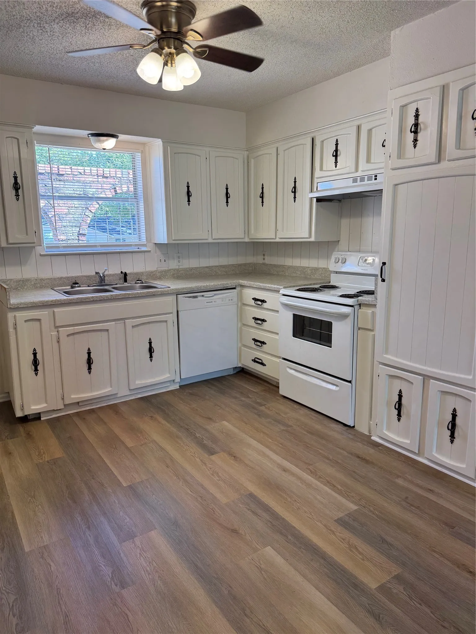 Kitchen featuring Luxury Vinyl Plank flooring, white cabinetry with decorative hardware, and integrated appliances