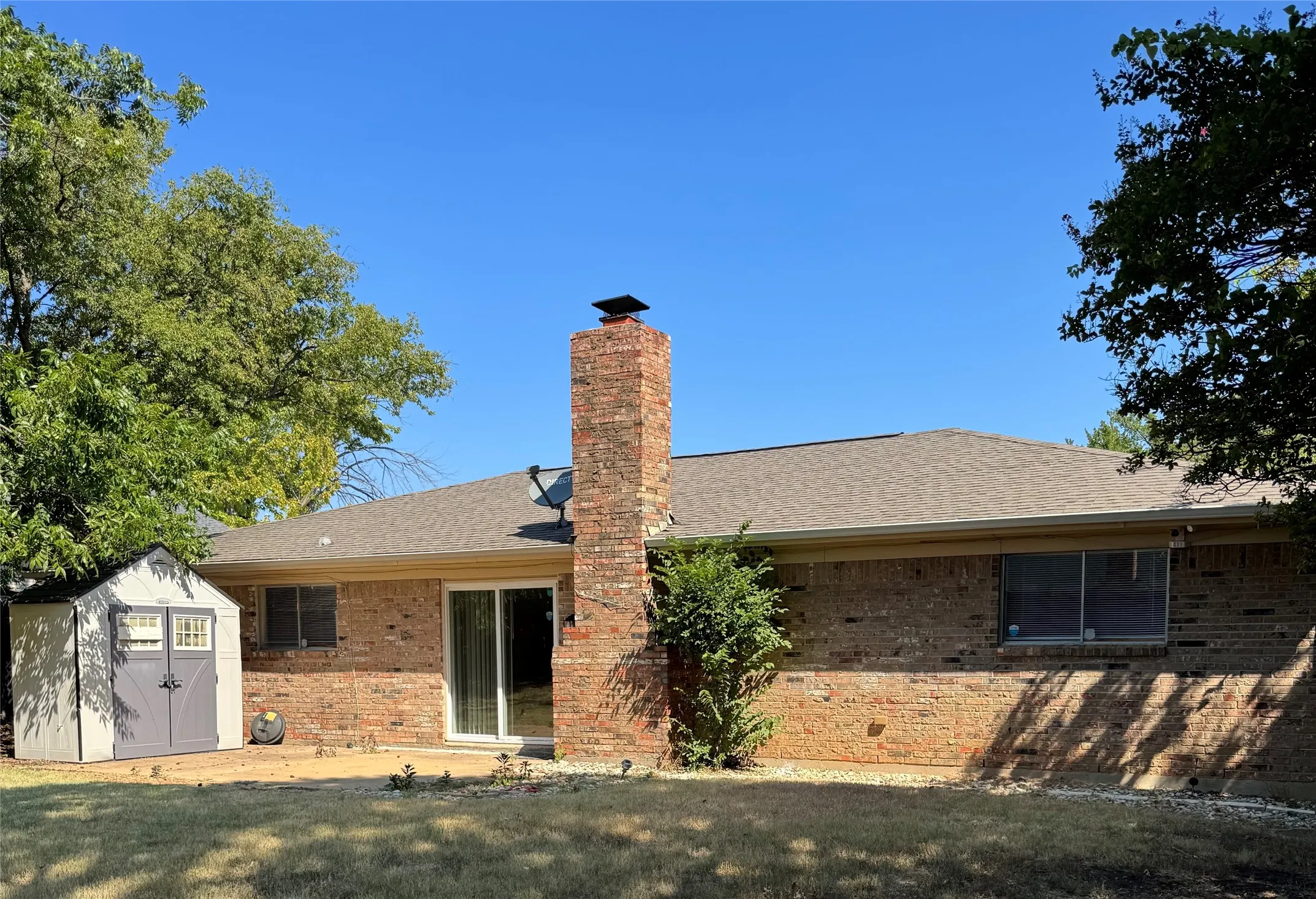 Brick exterior with a prominent chimney, storage building and a composite shingle roof