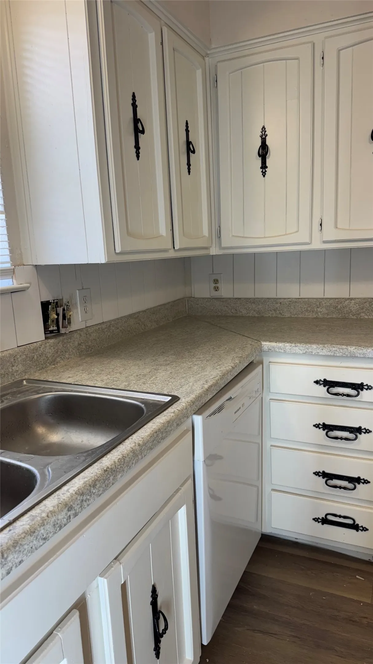 White cabinetry with decorative black hardware, double basin stainless steel sink, light-toned countertops, and a white dishwasher