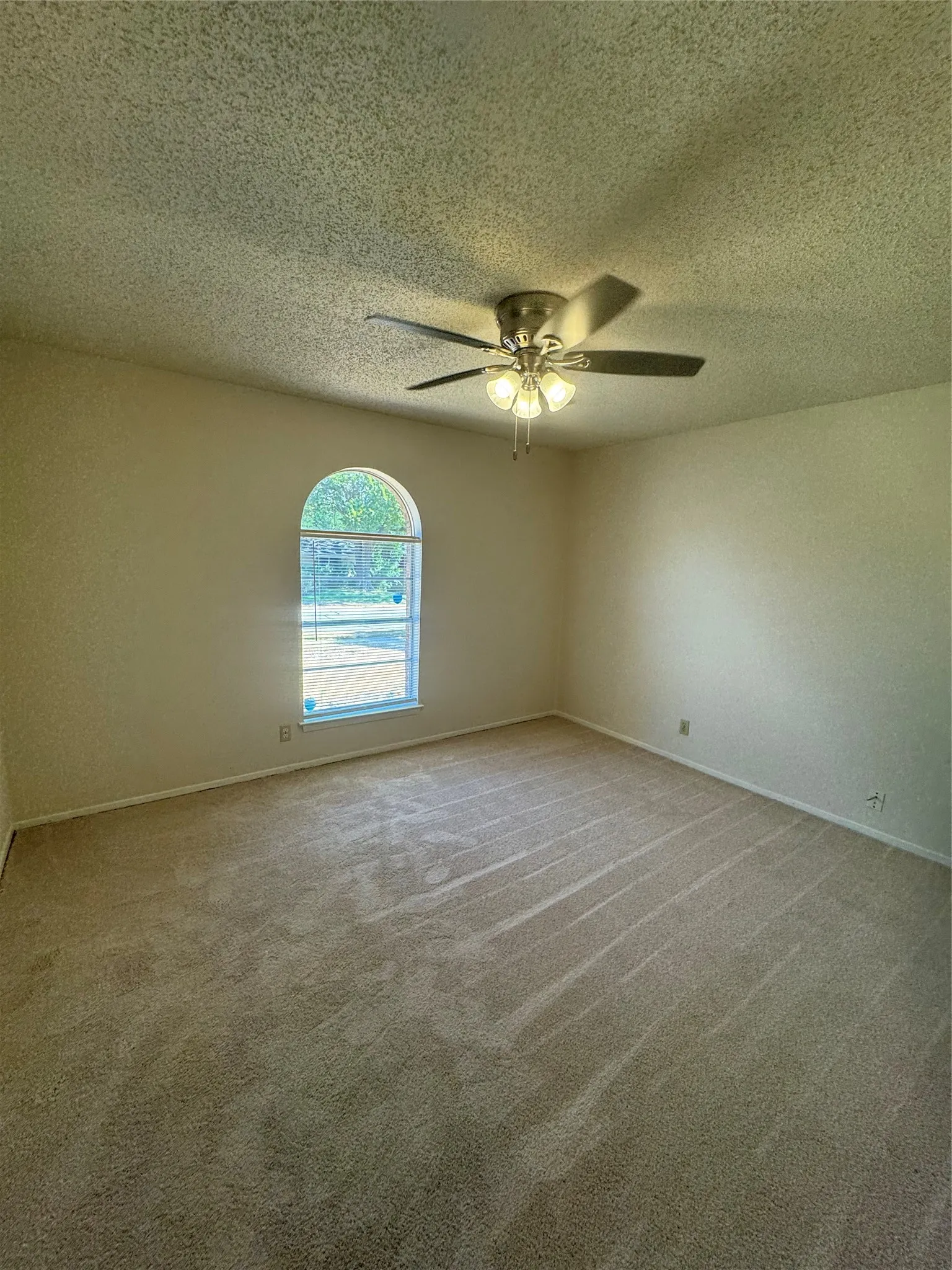 Arched window, ceiling fan with integrated lighting, carpeted flooring, and neutral wall tones