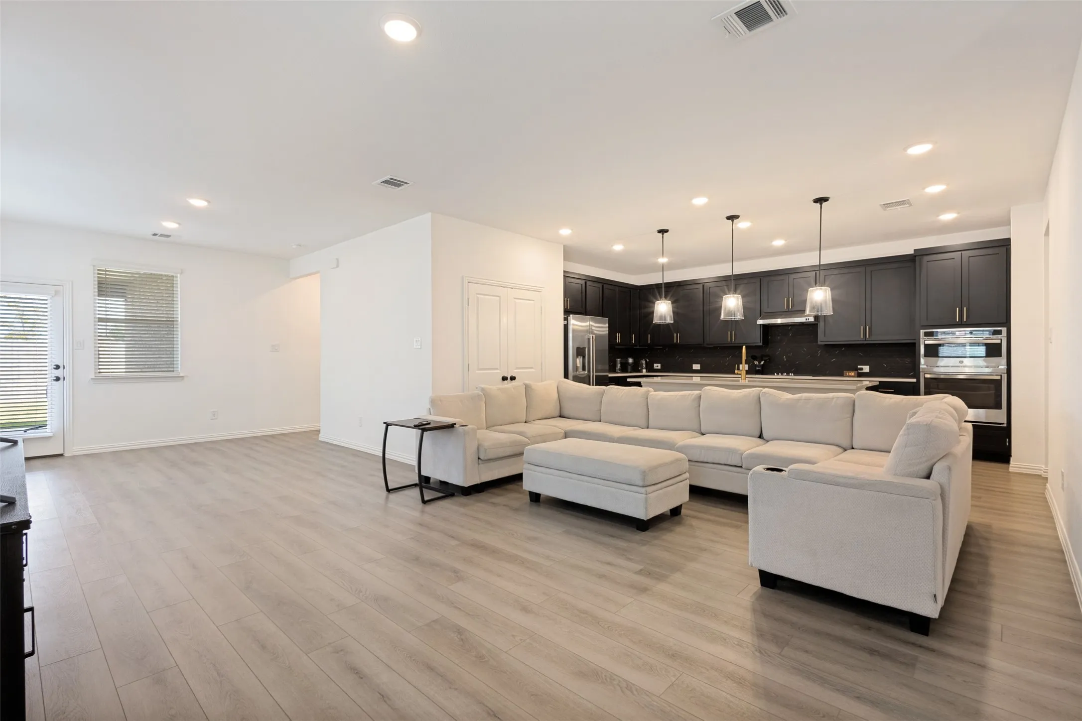 Open-concept floor plan featuring wood-finish flooring, recessed lighting, and a kitchen with dark cabinetry, stainless steel appliances, and pendant lighting