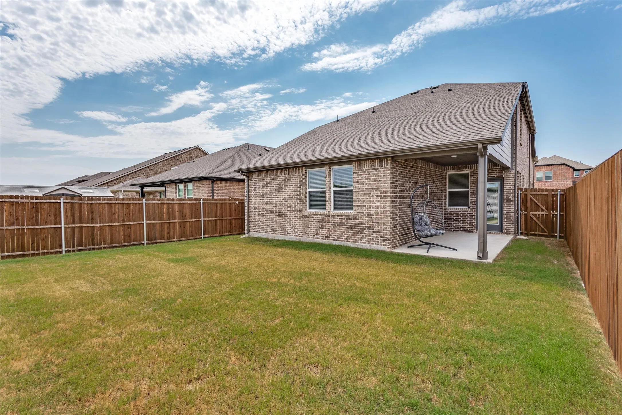 Expansive fenced backyard featuring a covered patio, brick exterior, and a side access gate