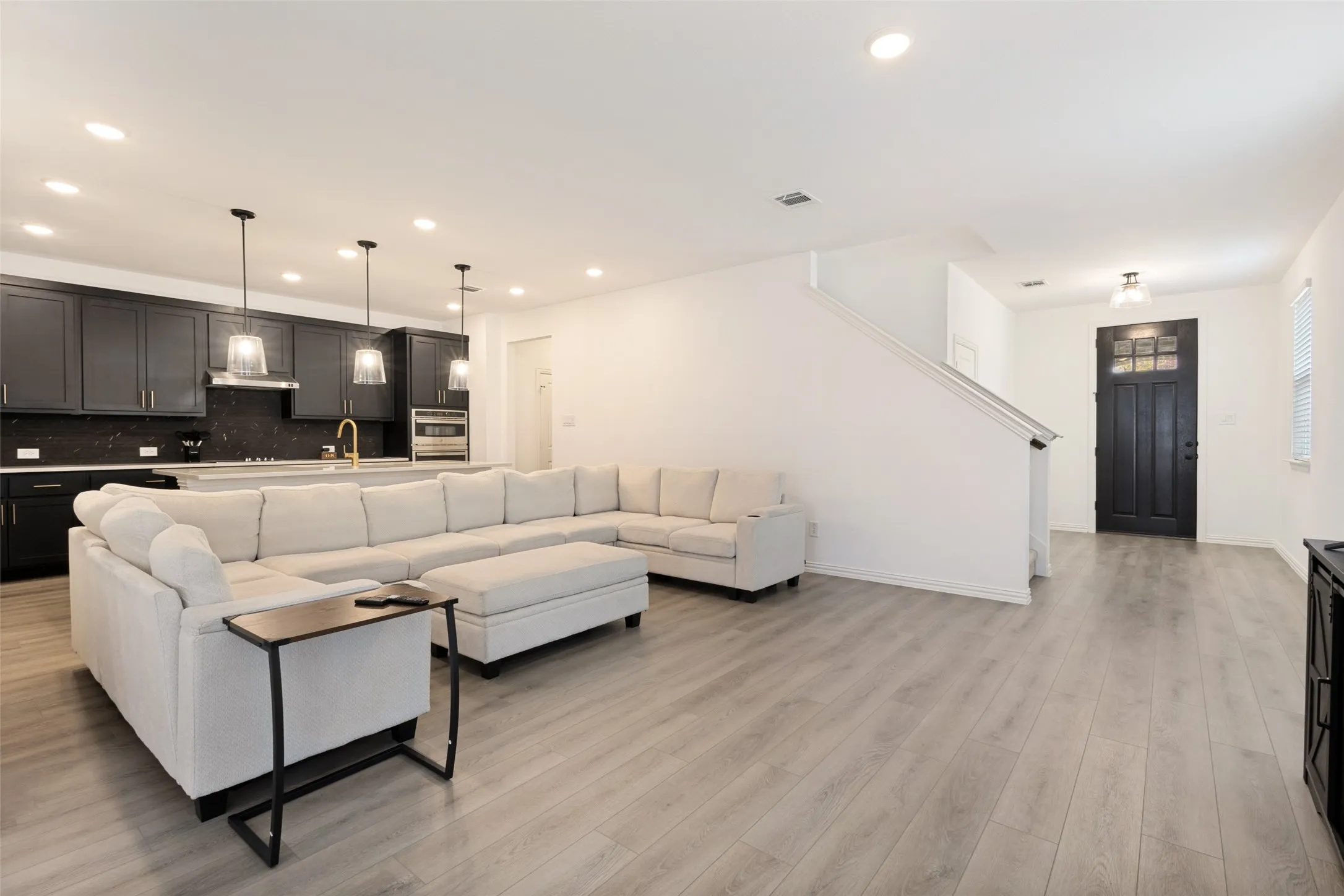 Open-concept living space with wood-finish flooring, recessed lighting, and a dark-paneled entry door