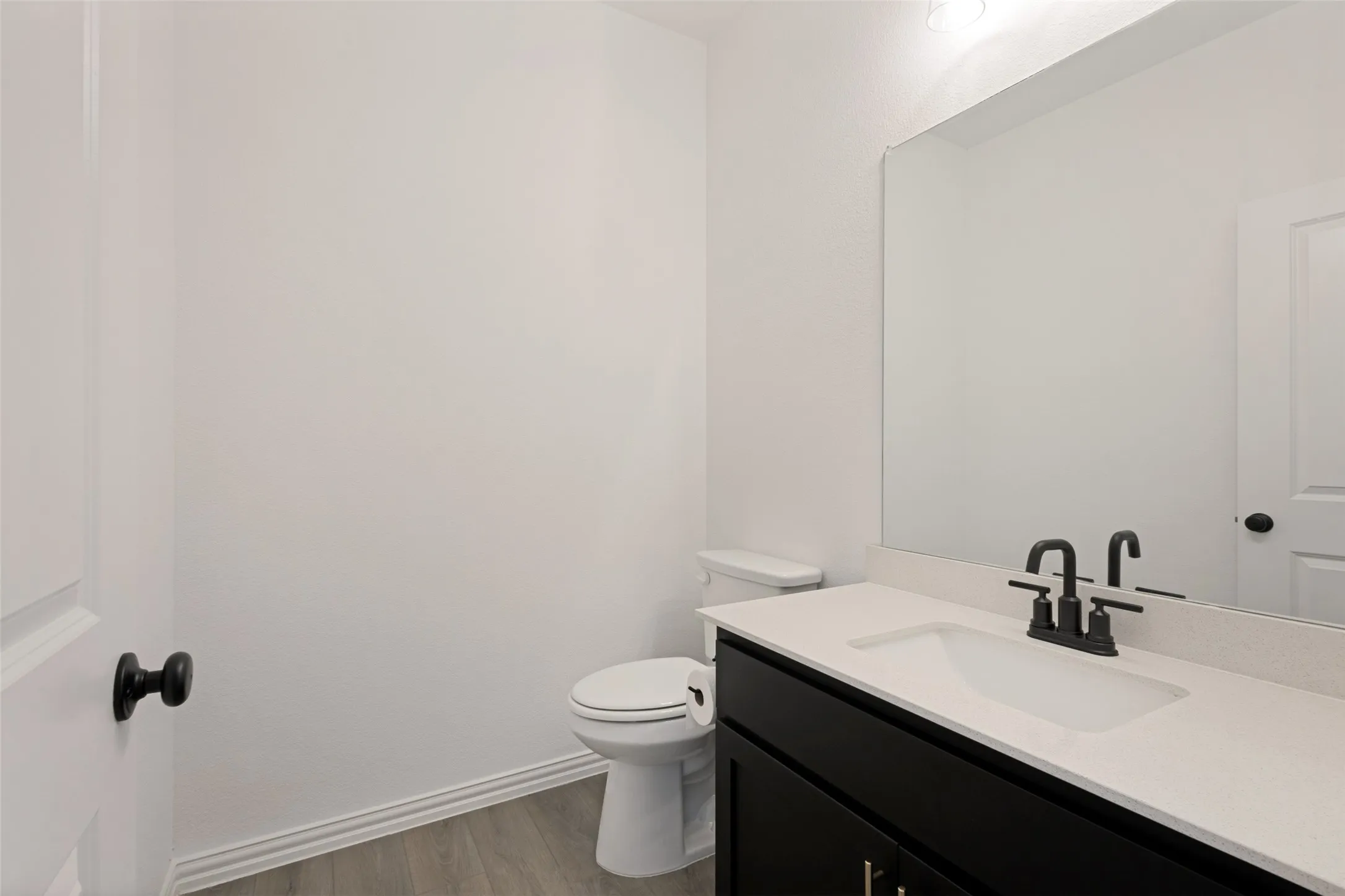 Vanity with a white countertop and integrated sink, matte black faucet, and wood-finish flooring
