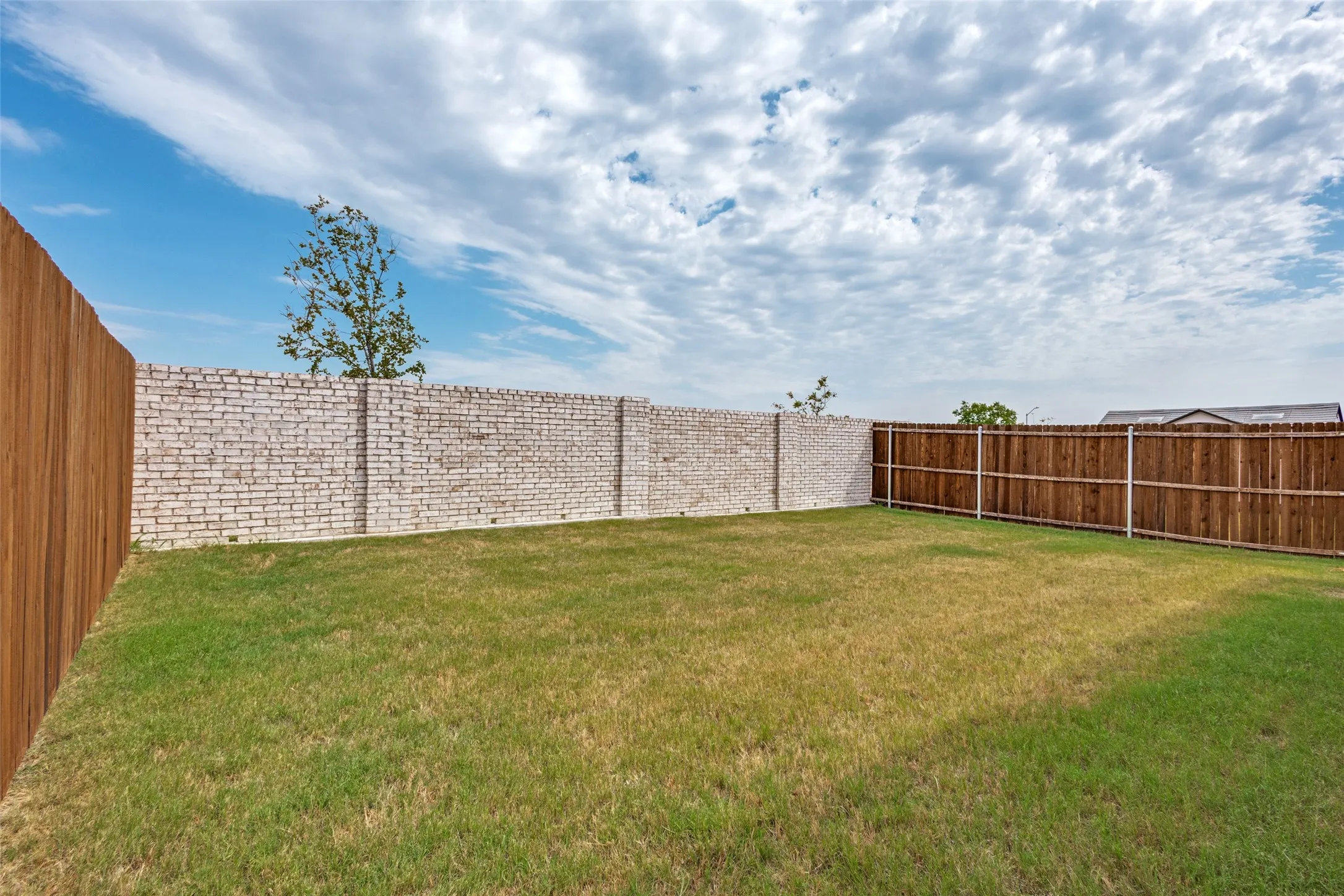 Expansive backyard featuring a manicured lawn, a full wooden privacy fence, and a decorative brick wall